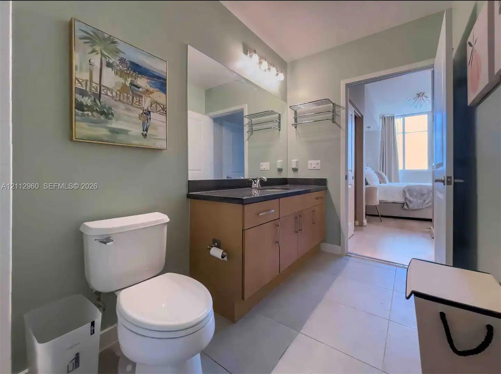 Bathroom featuring a vanity with light-tone cabinetry, dark surface countertop, integrated sink, wall-spanning vanity mirror, and multi-bulb fixed lighting