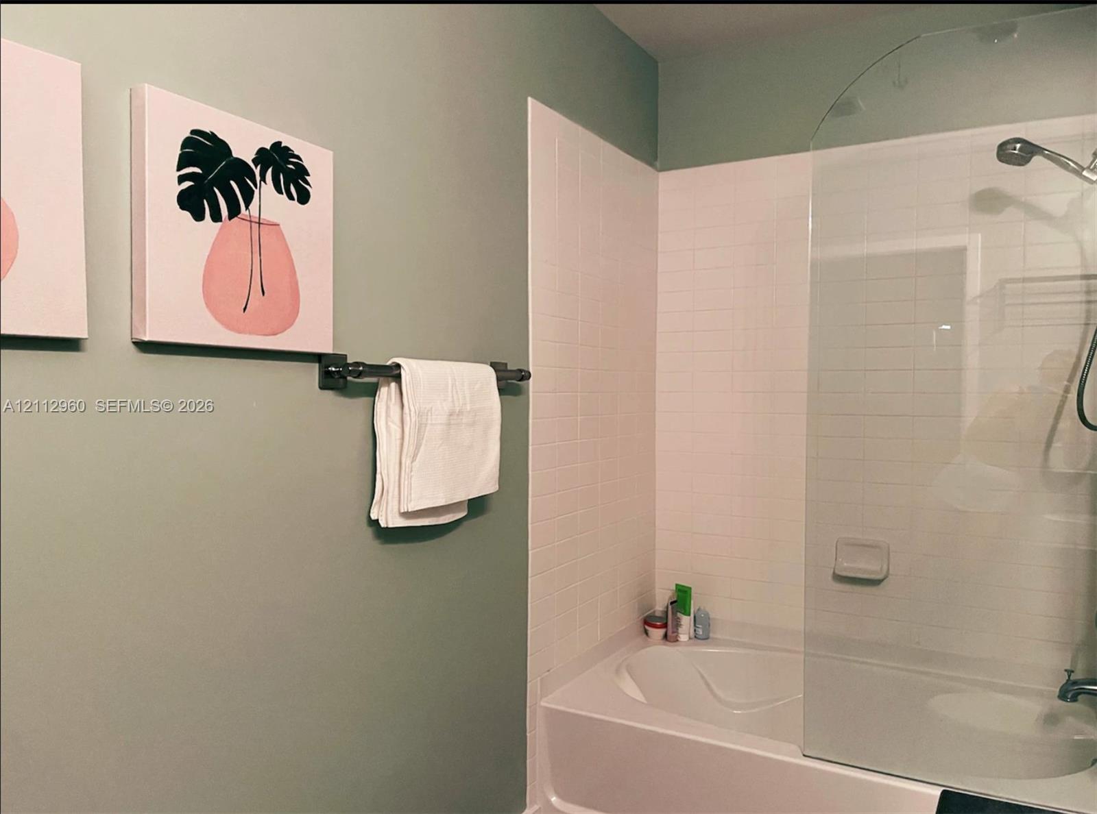 Soaking tub with white ceramic wall tile surround, curved glass panel enclosure, and oil-rubbed bronze finished wall-mounted towel bar