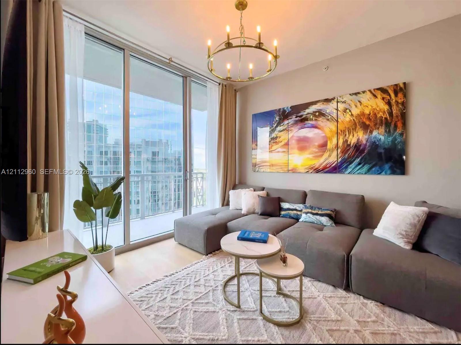 Floor-to-ceiling sliding glass doors, brass-finish circular chandelier, and neutral wall tones Floor-to-ceiling sliding glass doors, brass-finish circular chandelier, and neutral wall tones