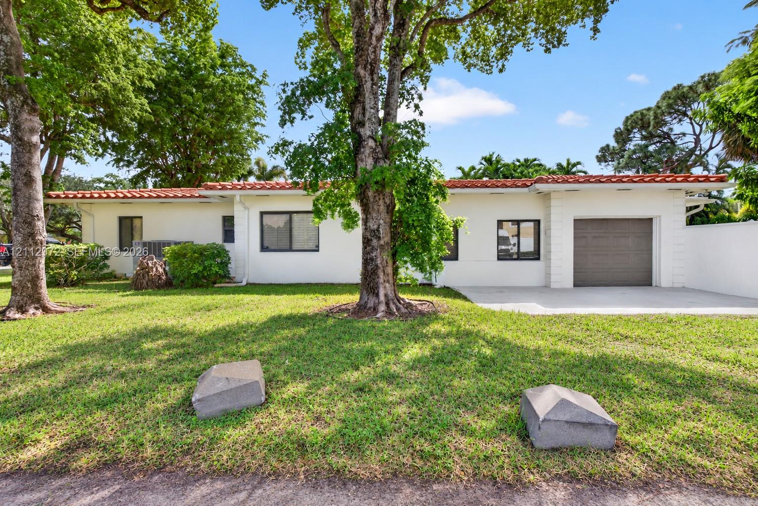 Stucco exterior featuring a terracotta tile roof, single-car garage, and mature trees on a landscaped lot Stucco exterior featuring a terracotta tile roof, single-car garage, and mature trees on a landscaped lot
