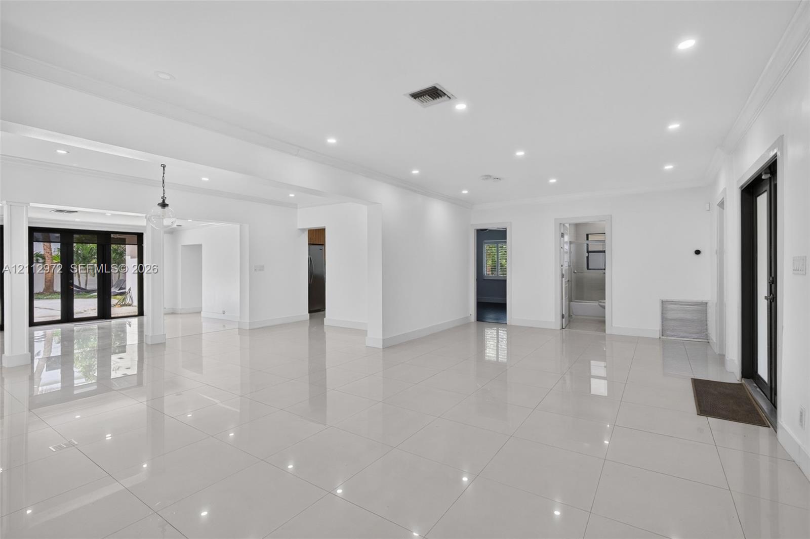 Open-concept interior featuring large-format tile flooring, recessed ceiling lighting, crown molding, and black-framed glass patio doors Open-concept interior featuring large-format tile flooring, recessed ceiling lighting, crown molding, and black-framed glass patio doors