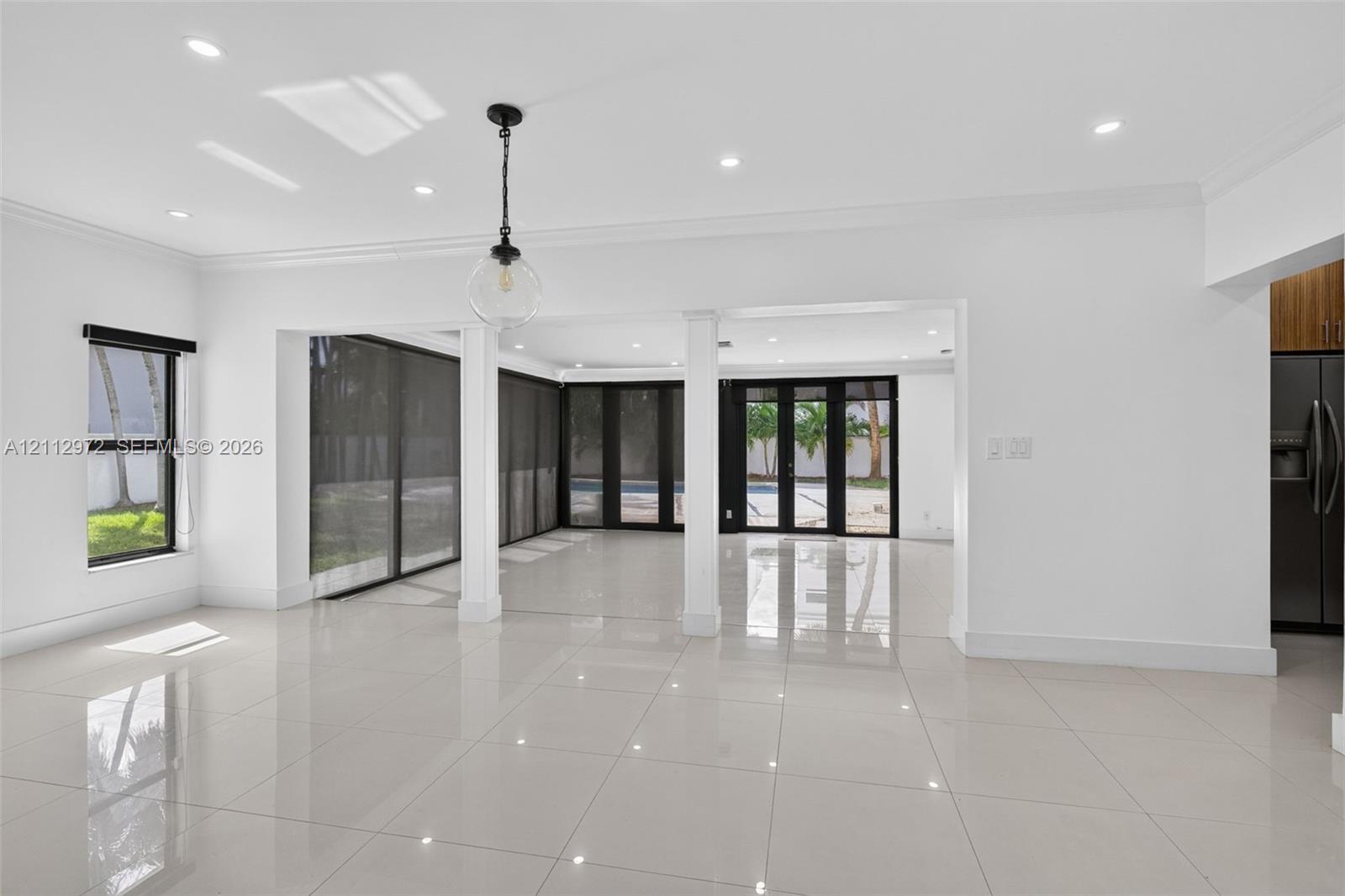 Large-format polished tile flooring, recessed ceiling lighting, structural support columns, black-framed sliding glass doors, and a decorative globe pendant fixture Large-format polished tile flooring, recessed ceiling lighting, structural support columns, black-framed sliding glass doors, and a decorative globe pendant fixture