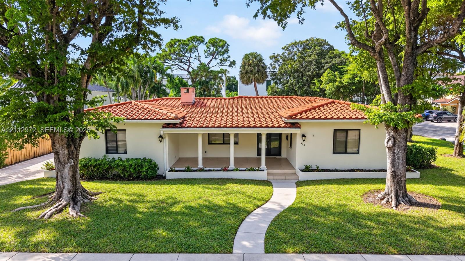 Single-story residence featuring a tile roof, covered front porch, stucco exterior, mature trees, and a manicured lawn Single-story residence featuring a tile roof, covered front porch, stucco exterior, mature trees, and a manicured lawn