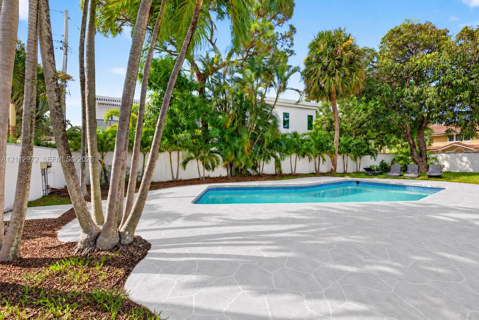 Outdoor space featuring a swimming pool, expansive stone-paver patio, perimeter privacy fencing, and mature palm trees