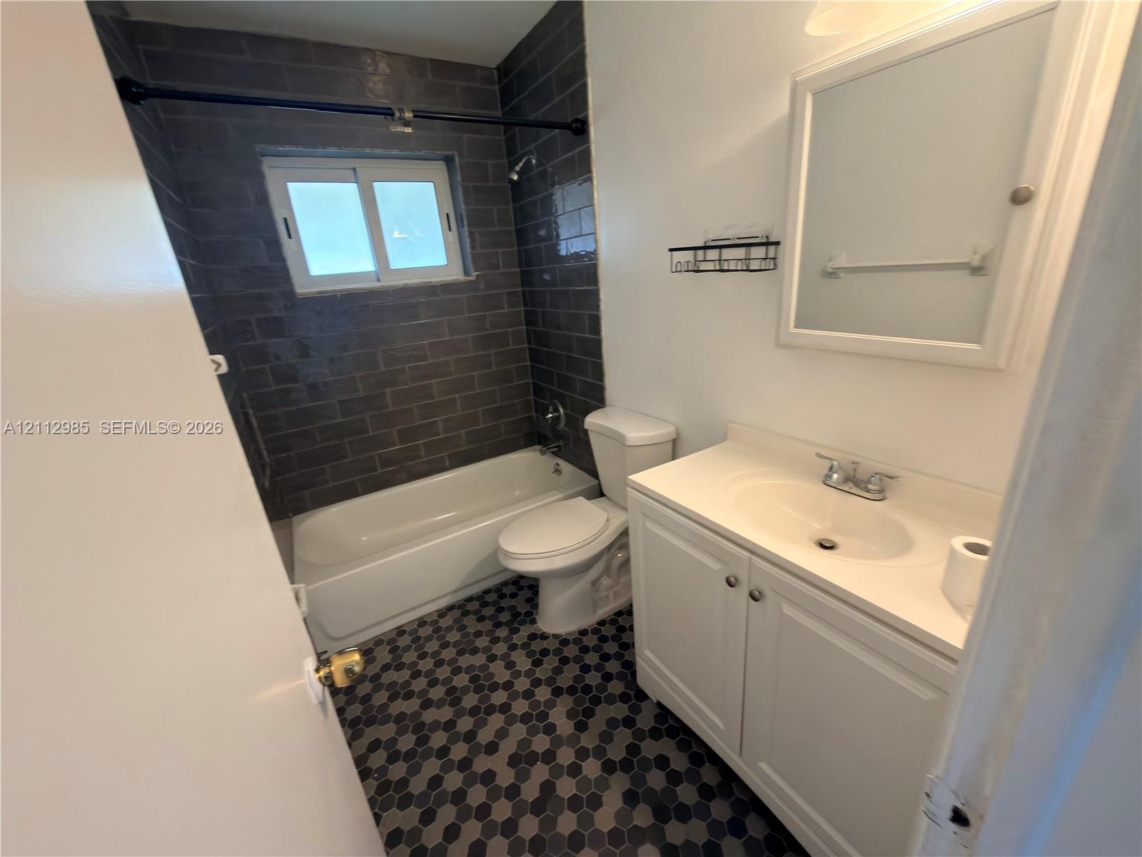 Bathroom featuring dark subway tile shower surround, hexagonal floor tile, white vanity with integrated sink, and medicine cabinet with integrated lighting