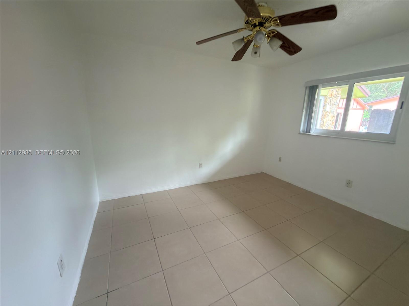 Neutral-toned ceramic tile flooring, clean white wall finishes, sliding glass window, and a ceiling-mounted light fixture with a fan