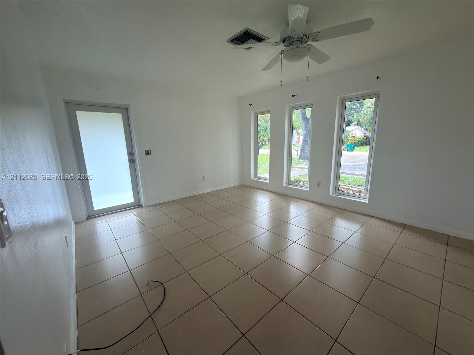 Interior space featuring large-format ceramic tile flooring, three floor-to-ceiling windows, an exterior glass-panel door, and a ceiling-mounted fan
