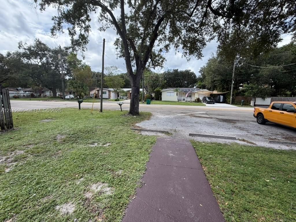 Corner lot featuring a paved walkway, gravel parking area, mature trees, and expansive lawn space Corner lot featuring a paved walkway, gravel parking area, mature trees, and expansive lawn space