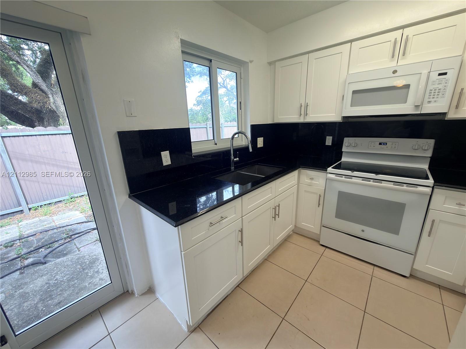 Kitchen featuring white cabinetry, dark stone-finish countertops, black backsplash, white appliance suite, and ceramic tile flooring Kitchen featuring white cabinetry, dark stone-finish countertops, black backsplash, white appliance suite, and ceramic tile flooring