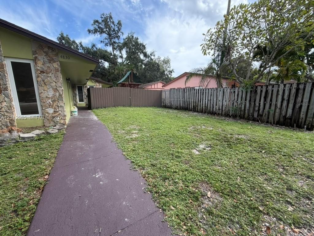 Exterior of residence featuring natural stone veneer siding, concrete paved walkway, and grass lawn enclosed by vertical wood fencing Exterior of residence featuring natural stone veneer siding, concrete paved walkway, and grass lawn enclosed by vertical wood fencing