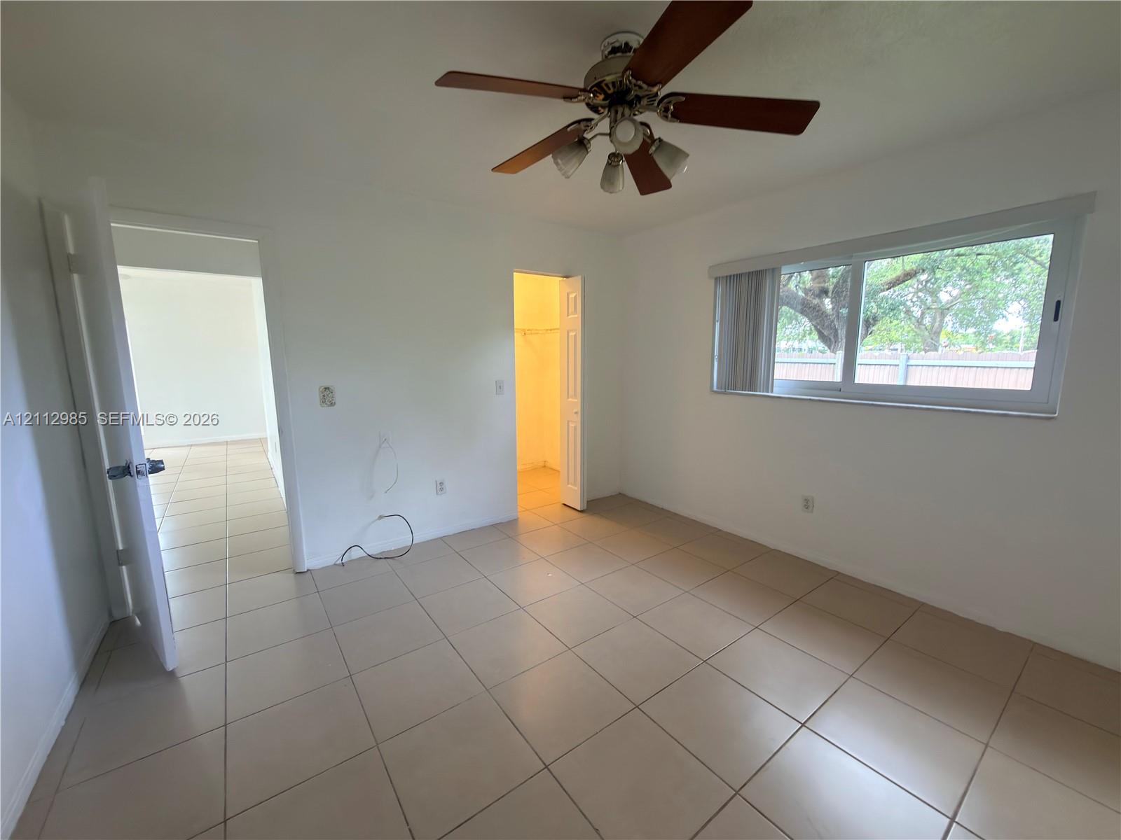 Room featuring neutral tile flooring, a horizontal sliding window with blinds, and a central ceiling fan with integrated lighting