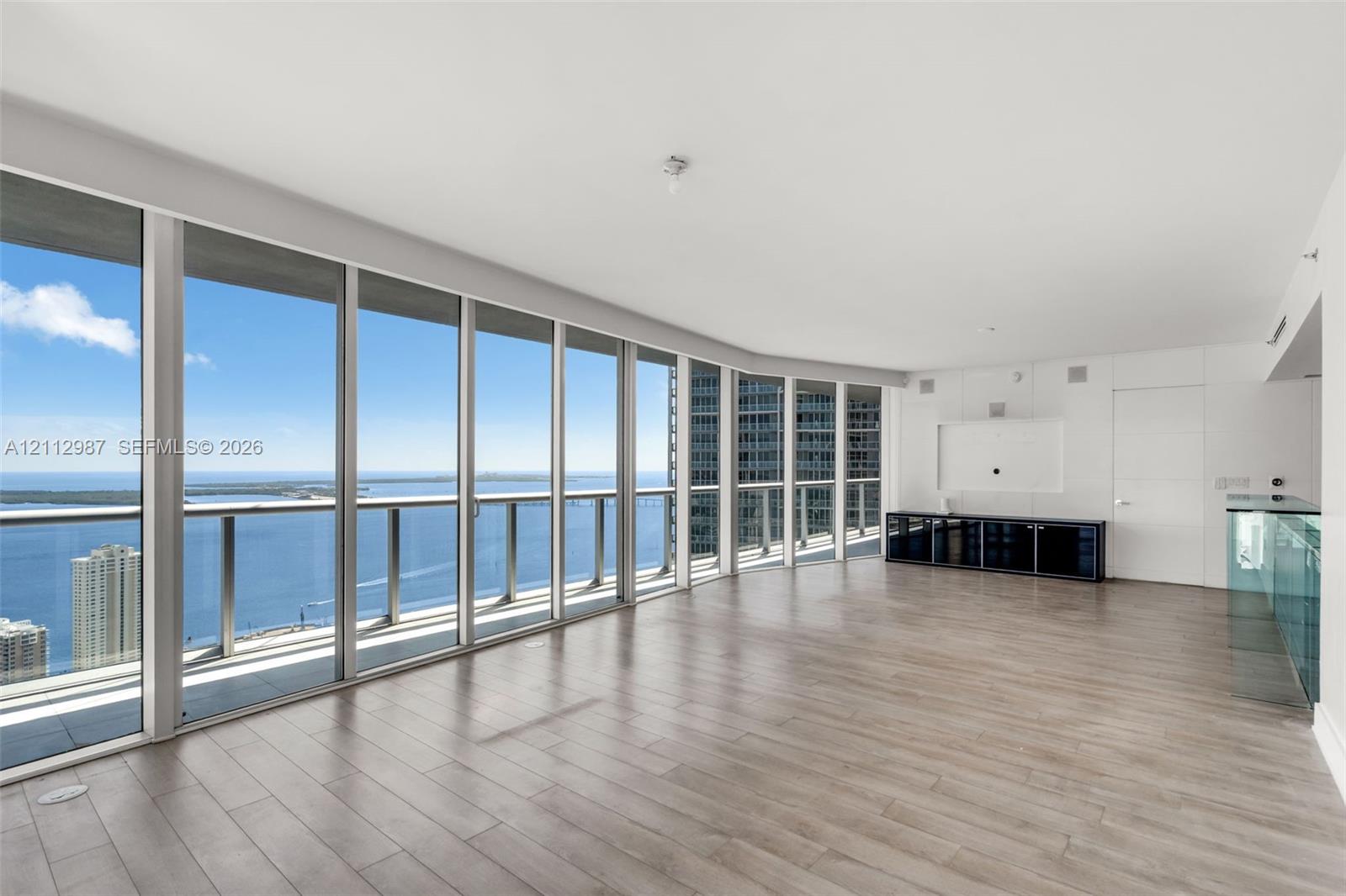 Floor-to-ceiling glass windows, wide-plank wood-finish flooring, and glass-railing balcony featuring expansive water and city skyline panoramas Floor-to-ceiling glass windows, wide-plank wood-finish flooring, and glass-railing balcony featuring expansive water and city skyline panoramas