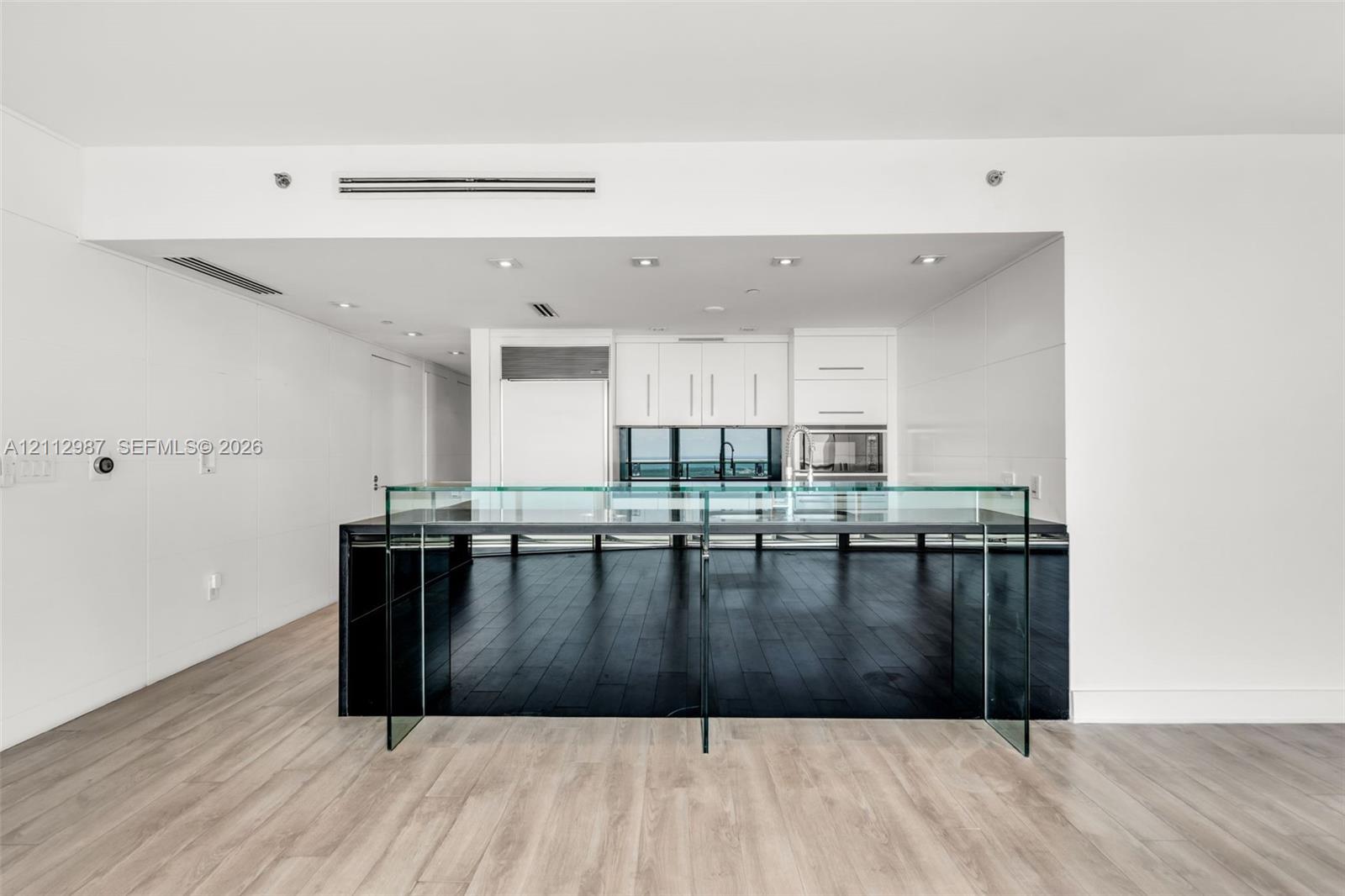 Kitchen featuring custom white cabinetry, integrated refrigerator, built-in microwave, minimalist glass-paneled island, and wood-finish flooring