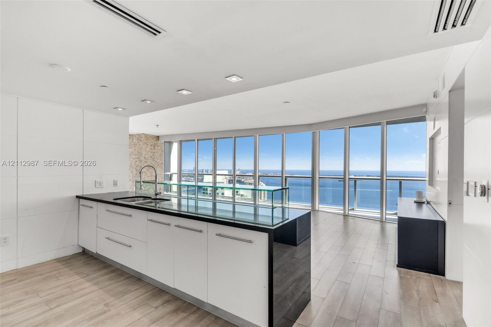 Kitchen featuring a central island with a dark stone countertop, integrated glass backsplash, white cabinetry with metal hardware, floor-to-ceiling windows, and wood-finish flooring