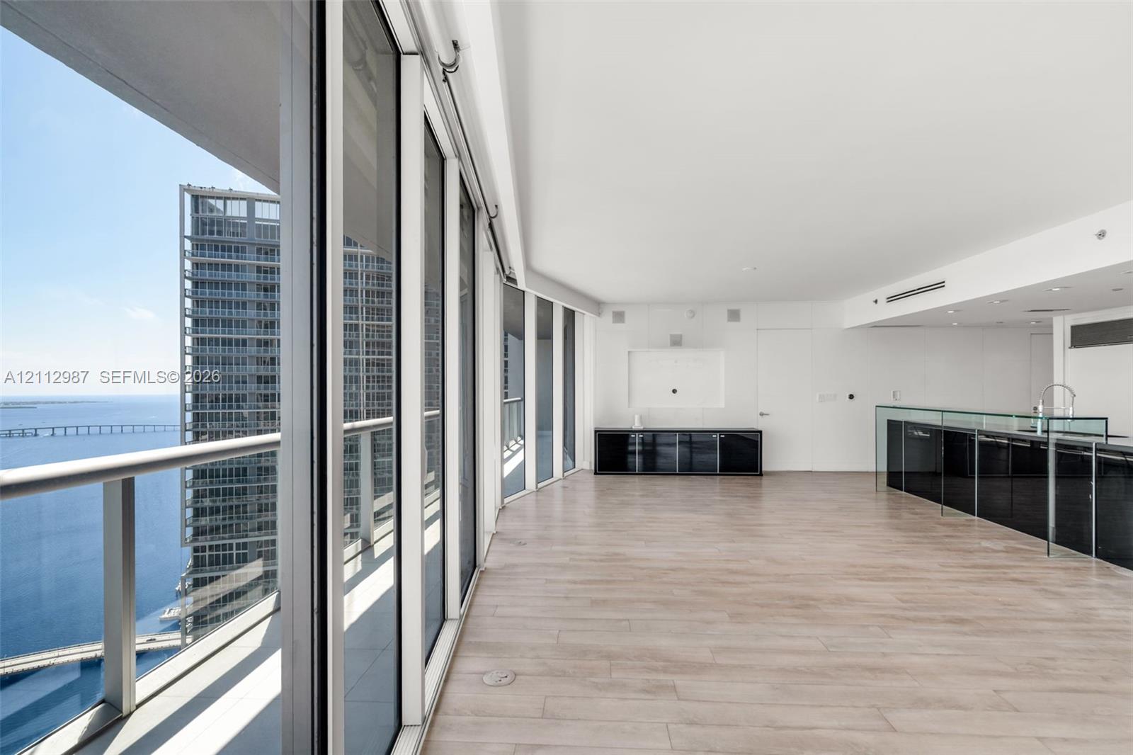 Floor-to-ceiling glass panel walls, wood-finish flooring, built-in black cabinetry, and a glass-partitioned kitchen area Floor-to-ceiling glass panel walls, wood-finish flooring, built-in black cabinetry, and a glass-partitioned kitchen area