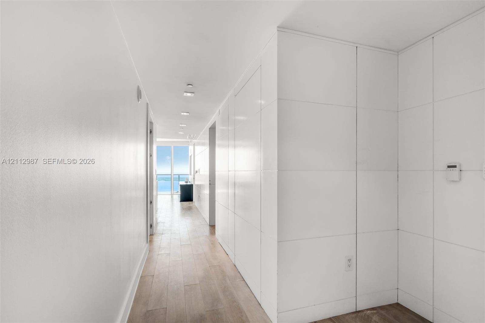 Hallway featuring wood-finish flooring, integrated floor-to-ceiling paneling, and recessed lighting Hallway featuring wood-finish flooring, integrated floor-to-ceiling paneling, and recessed lighting