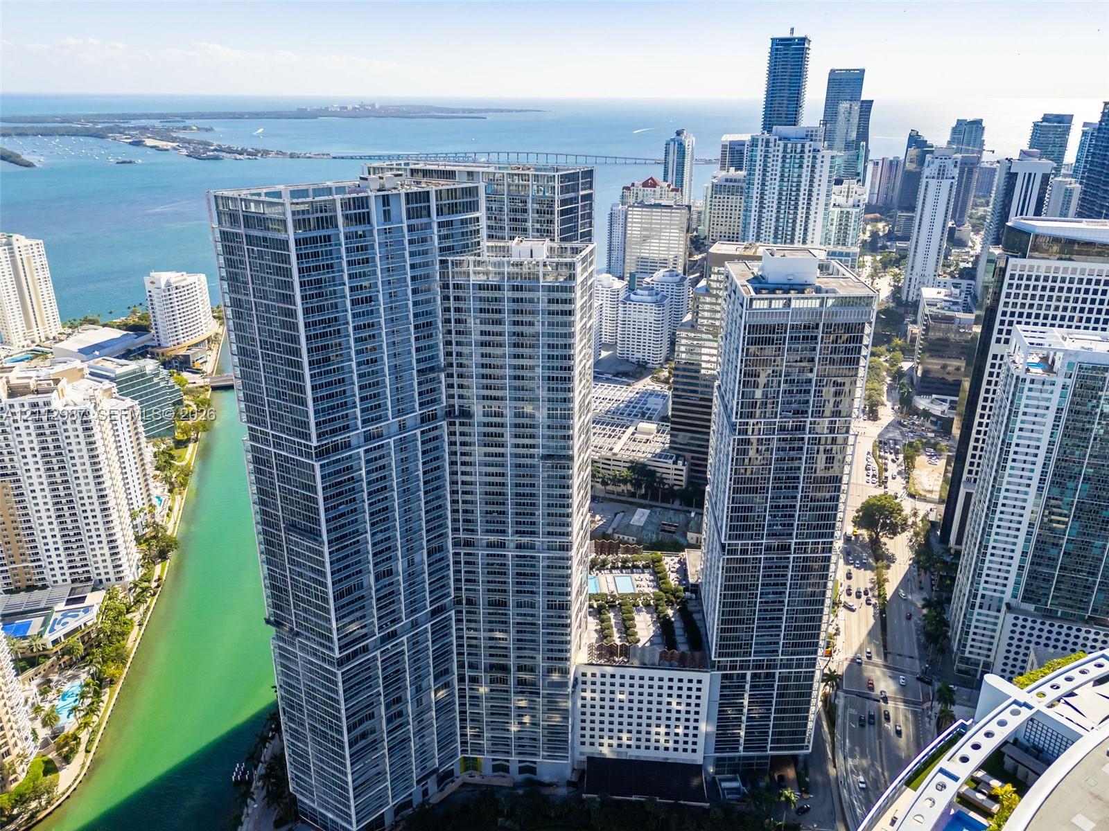 Aerial perspective featuring glass-facade high-rise towers, a multi-level podium with an elevated swimming pool and terrace, and proximity to the waterfront and urban cityscape
