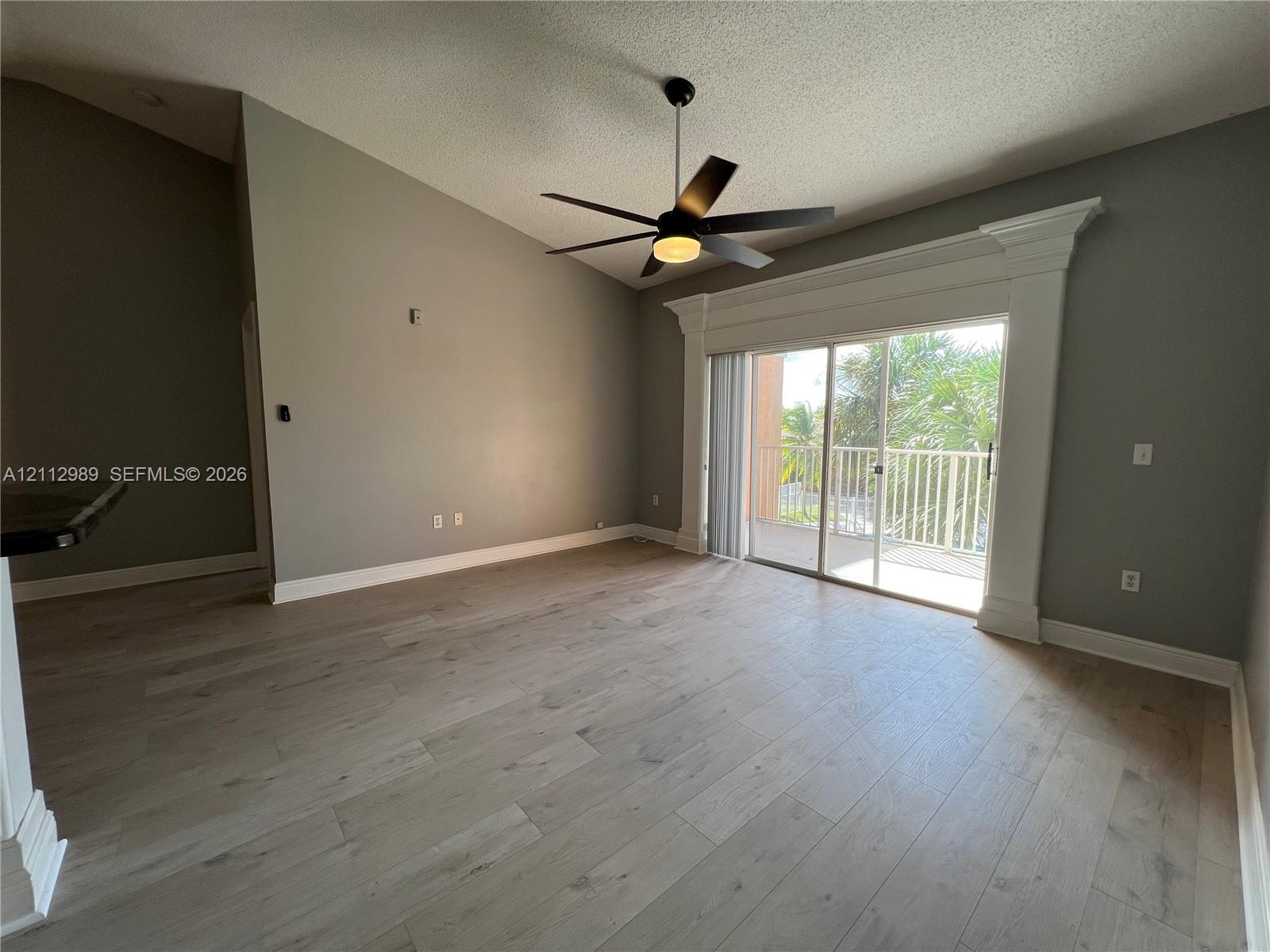 Vaulted ceilings, wood-finish flooring, central ceiling fan, and sliding glass doors encased in decorative molding with access to an exterior balcony