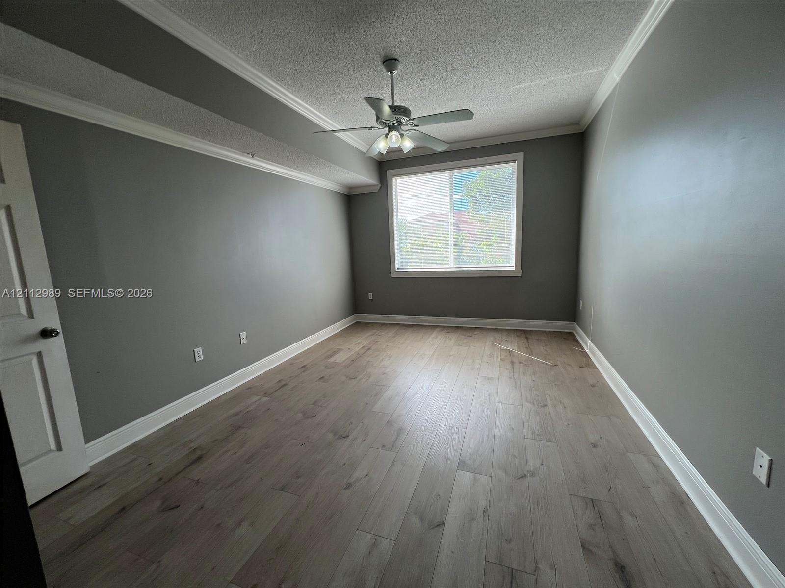 Room featuring wood-finish flooring, crown molding, a ceiling fan with integrated lighting, and a single-pane window