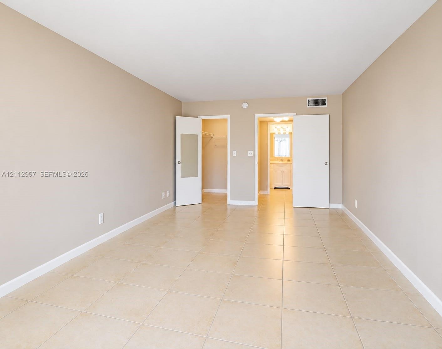 Neutral-toned room featuring large-format ceramic tile flooring, two white interior doors, and a walk-in closet Neutral-toned room featuring large-format ceramic tile flooring, two white interior doors, and a walk-in closet