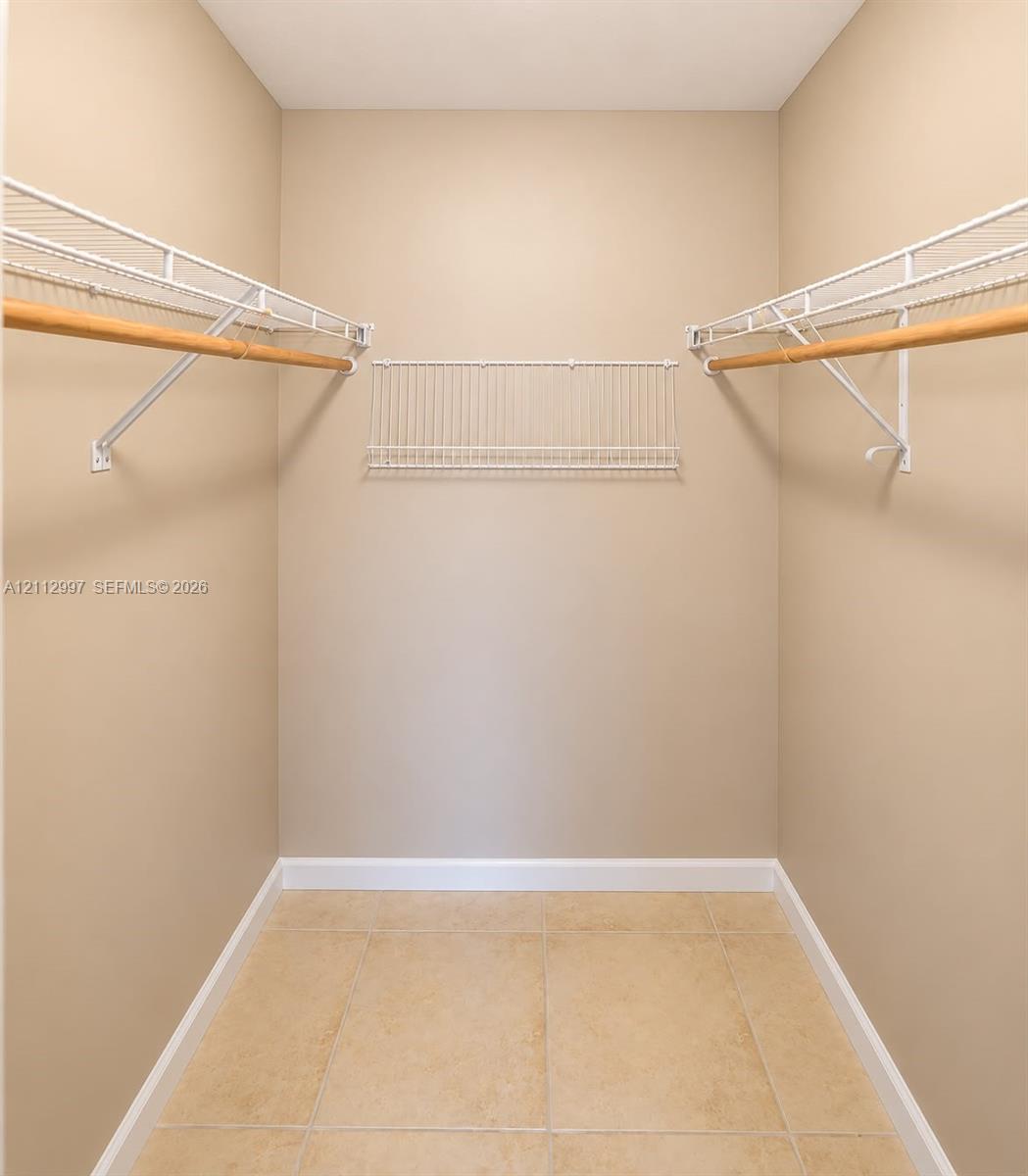 Walk-in storage space featuring ceramic tile flooring and multi-level white wire shelving with wood-finish garment rods Walk-in storage space featuring ceramic tile flooring and multi-level white wire shelving with wood-finish garment rods
