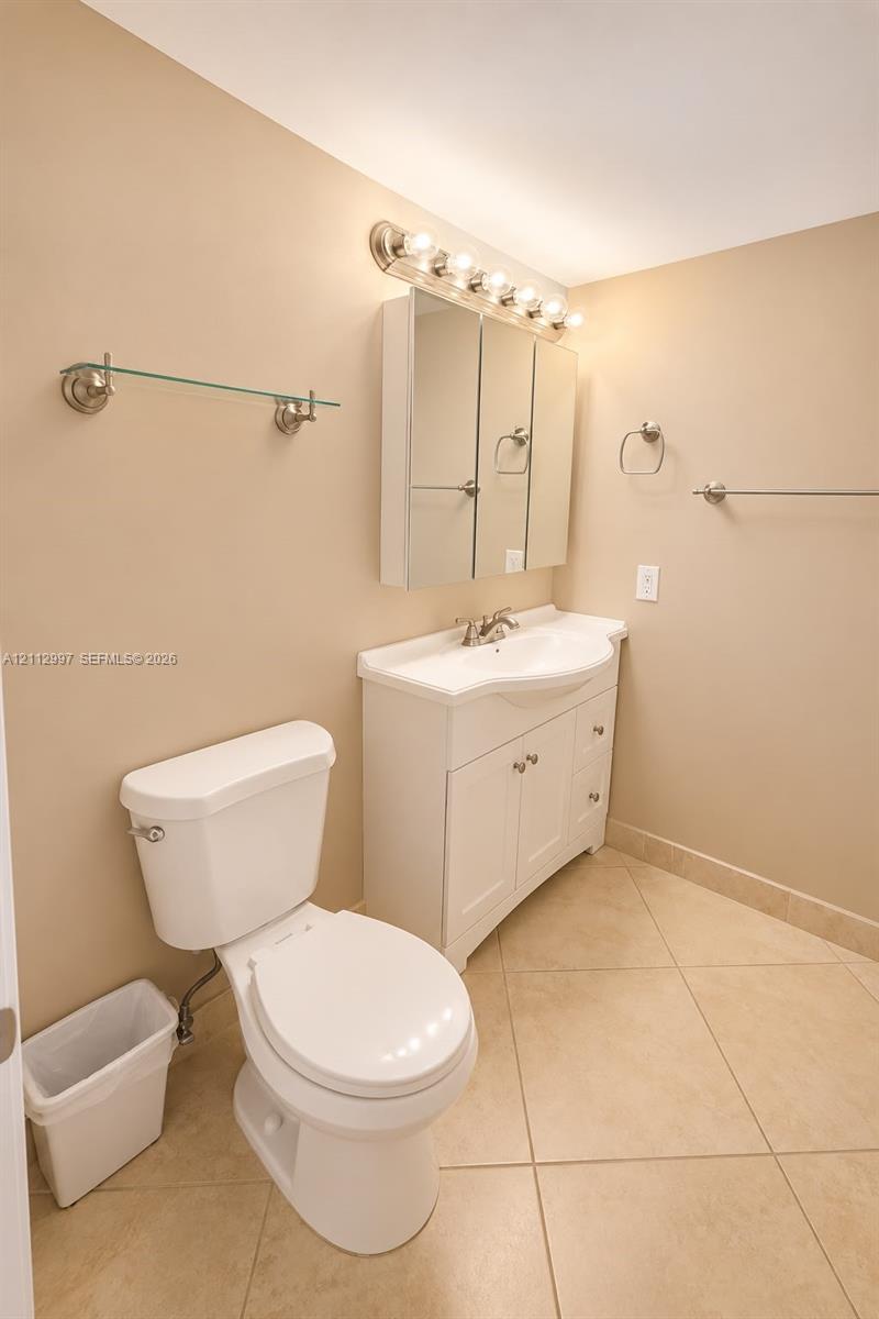 White vanity cabinet with an integrated sink, three-door mirrored medicine cabinet, multi-bulb wall-mounted lighting fixture, and neutral tile flooring White vanity cabinet with an integrated sink, three-door mirrored medicine cabinet, multi-bulb wall-mounted lighting fixture, and neutral tile flooring