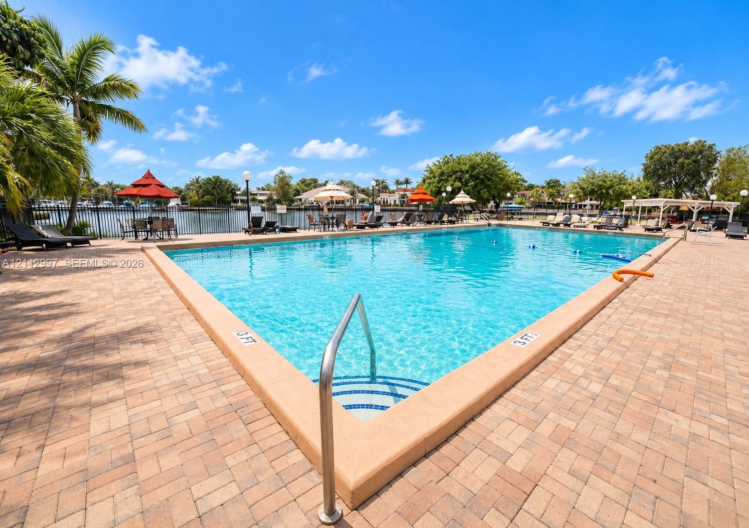 Large in-ground swimming pool featuring a brick paver deck, metal safety fencing, and stair entry Large in-ground swimming pool featuring a brick paver deck, metal safety fencing, and stair entry