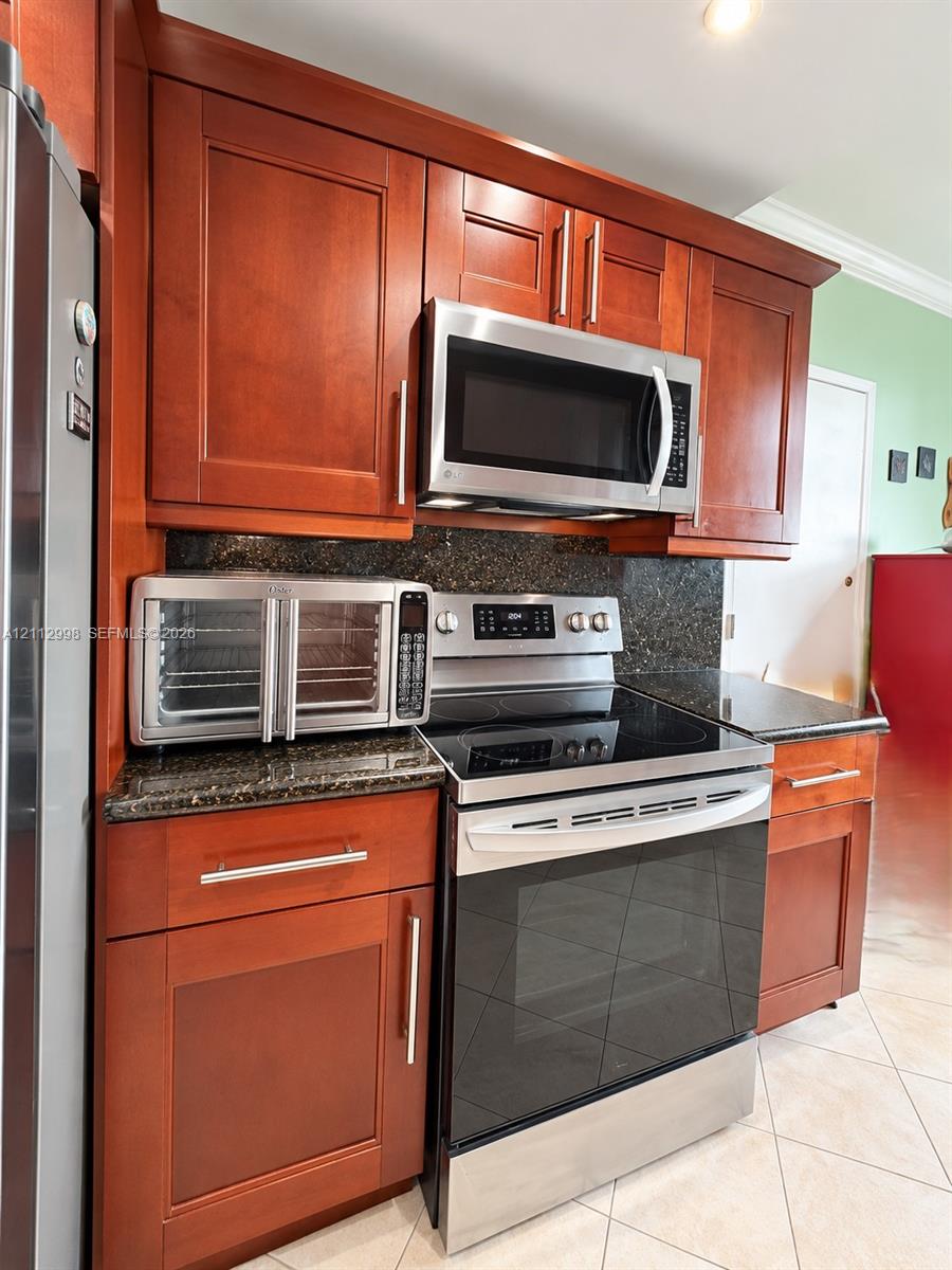 Kitchen featuring cherry-finish cabinetry, stone countertops, stainless steel microwave, and stainless steel range