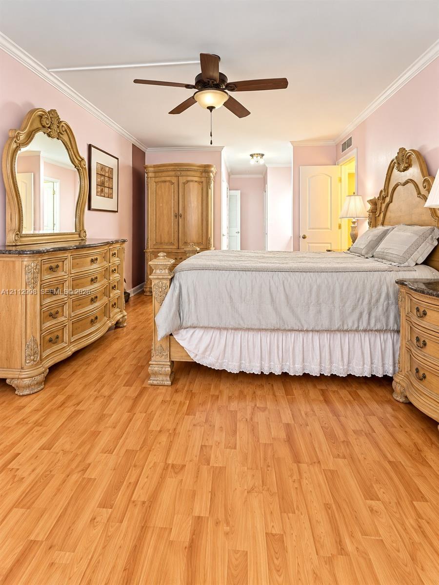 Interior space featuring wood-finish flooring, crown molding, a central ceiling fan with integrated lighting, and multi-panel interior doors