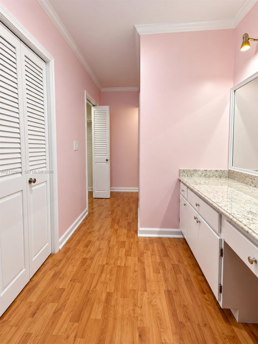 Dressing area featuring wood-finish flooring, white louvered-door cabinetry, stone-composite countertop, wall-mounted vanity lighting, and built-in closet storage