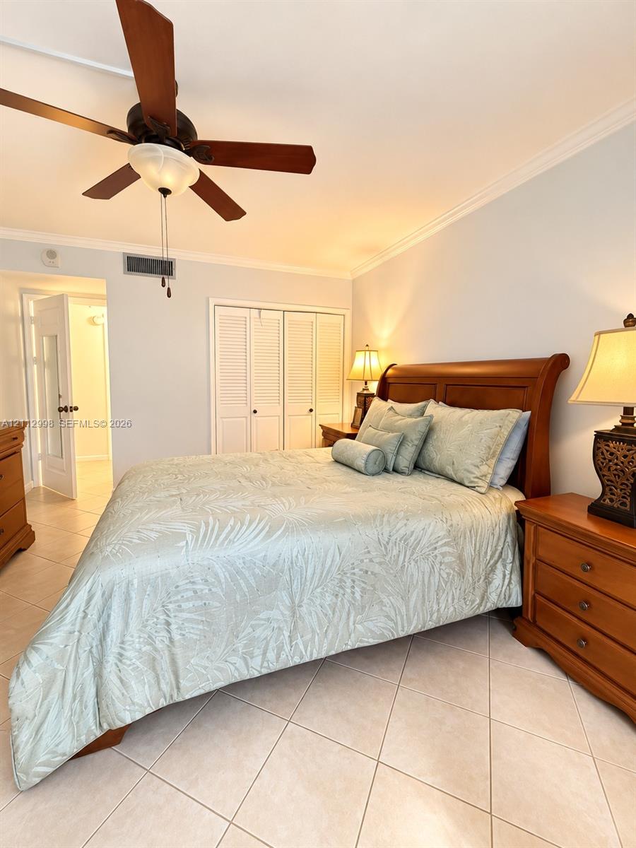 Ceramic tile flooring, crown molding, ceiling fan with light fixture, and closet with white louvered doors