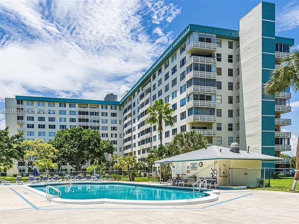 Multi-story condominium exterior featuring private balconies and an outdoor swimming pool with a surrounding concrete deck and detached cabana