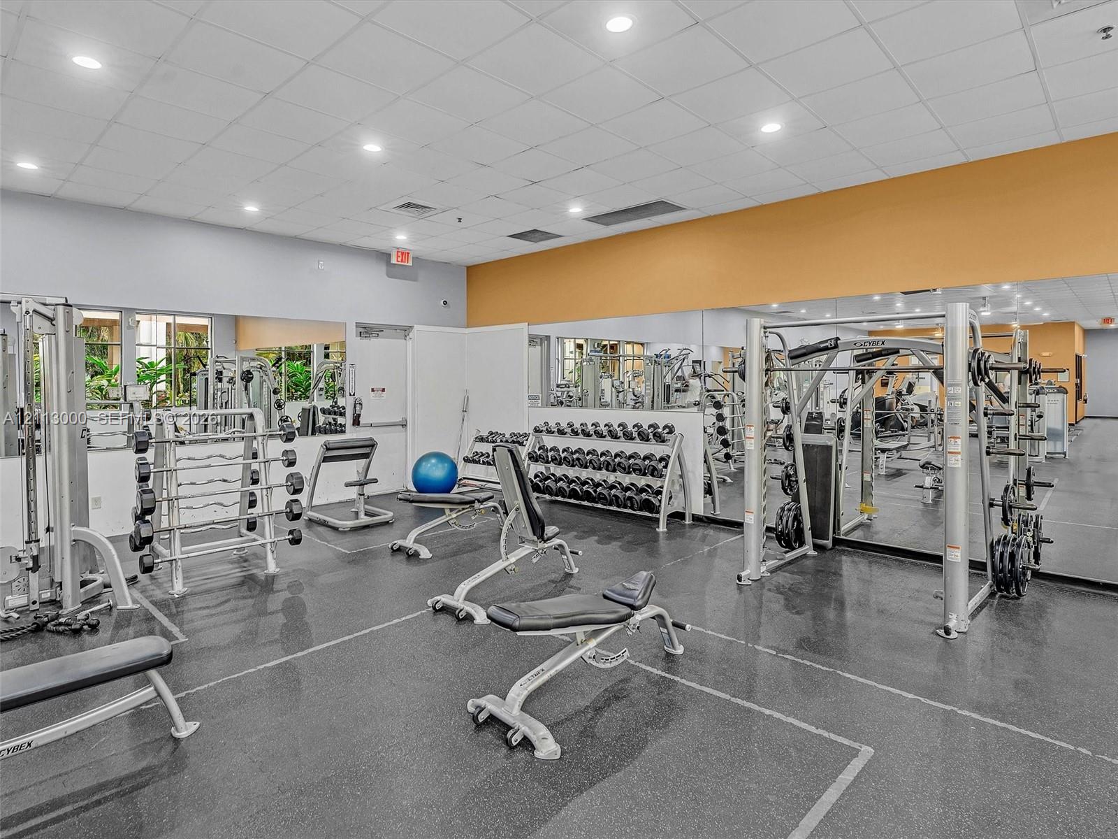 Fitness center featuring wall-to-wall mirrors, durable rubberized flooring, and recessed ceiling lighting