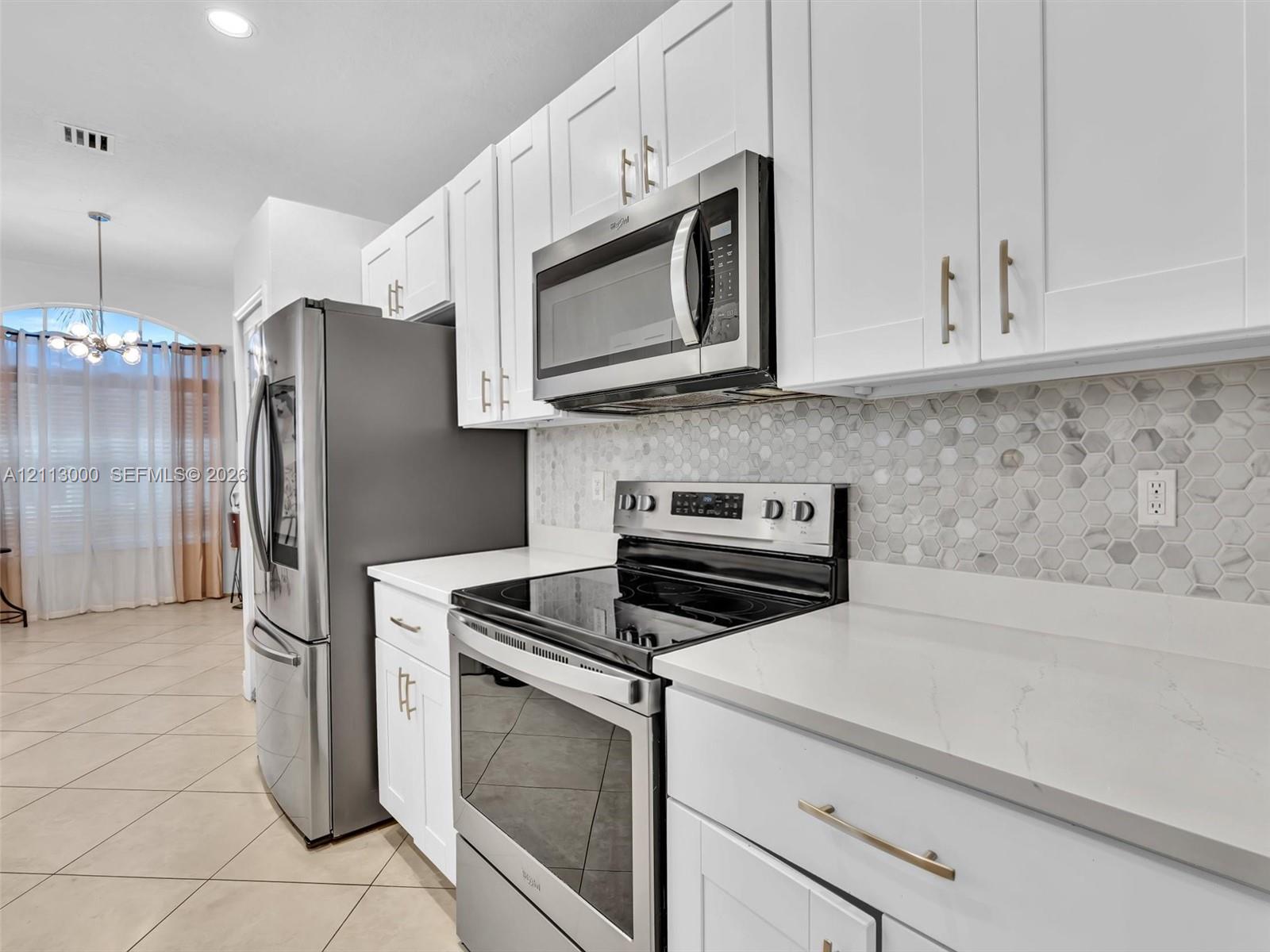 Kitchen featuring white shaker-style cabinetry, stainless steel appliances, quartz countertops, and a hexagonal tile backsplash