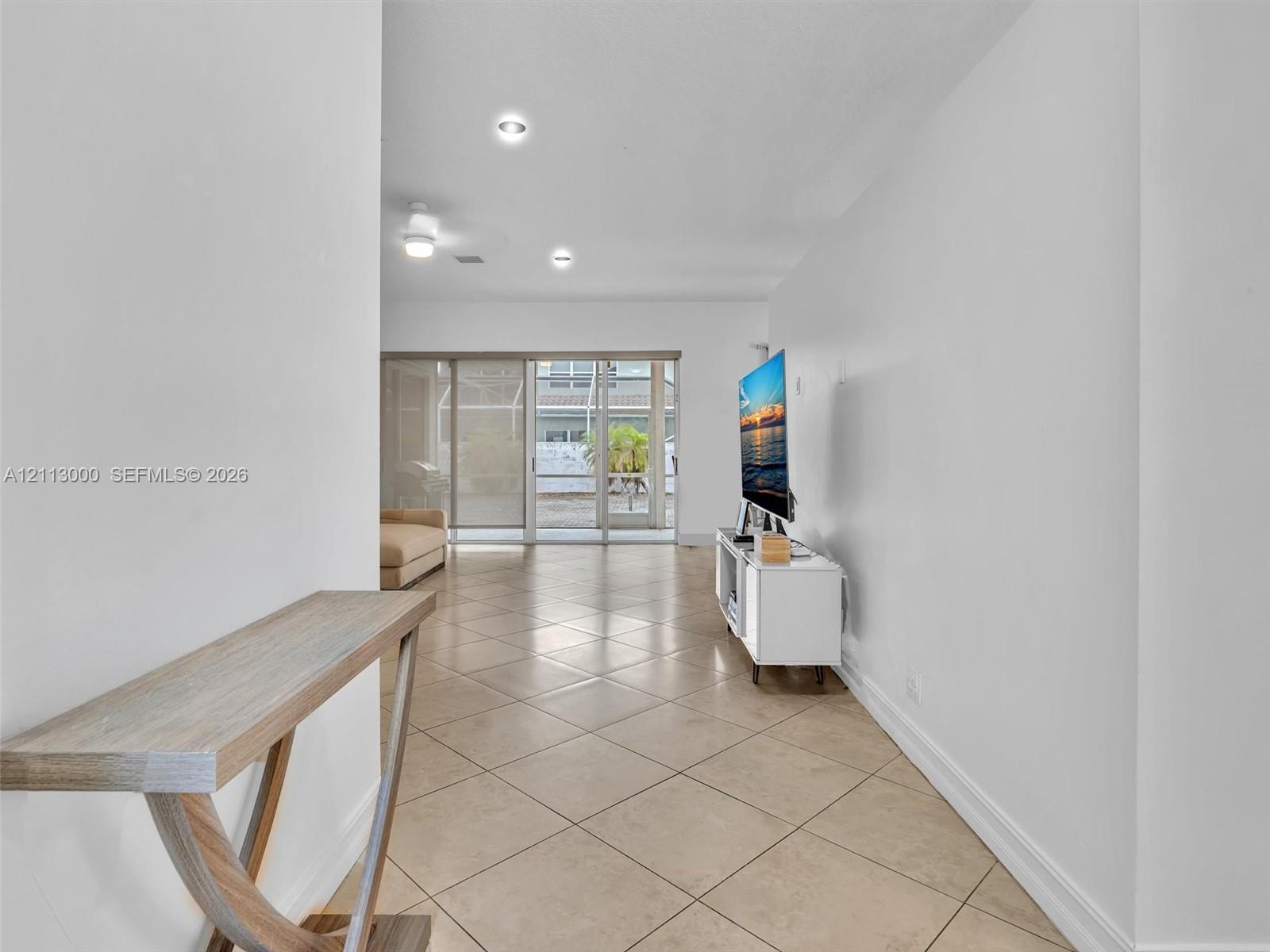 Neutral ceramic tile flooring, recessed ceiling lighting, and sliding glass doors leading to a screened-in enclosure