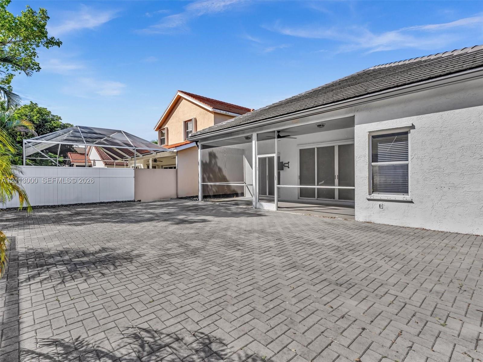 Exterior patio featuring a paved stone surface, a covered screened-in lanai, and white vinyl perimeter fencing