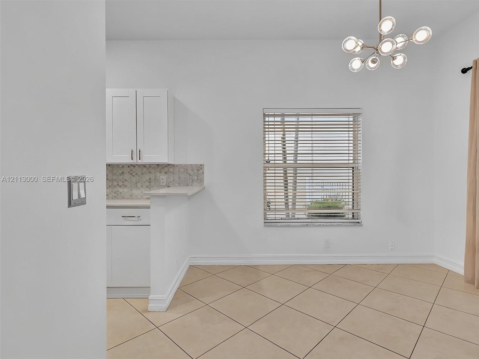 Modern multi-light pendant fixture, white shaker-style cabinetry, mosaic tile backsplash, and diagonal-set tile flooring