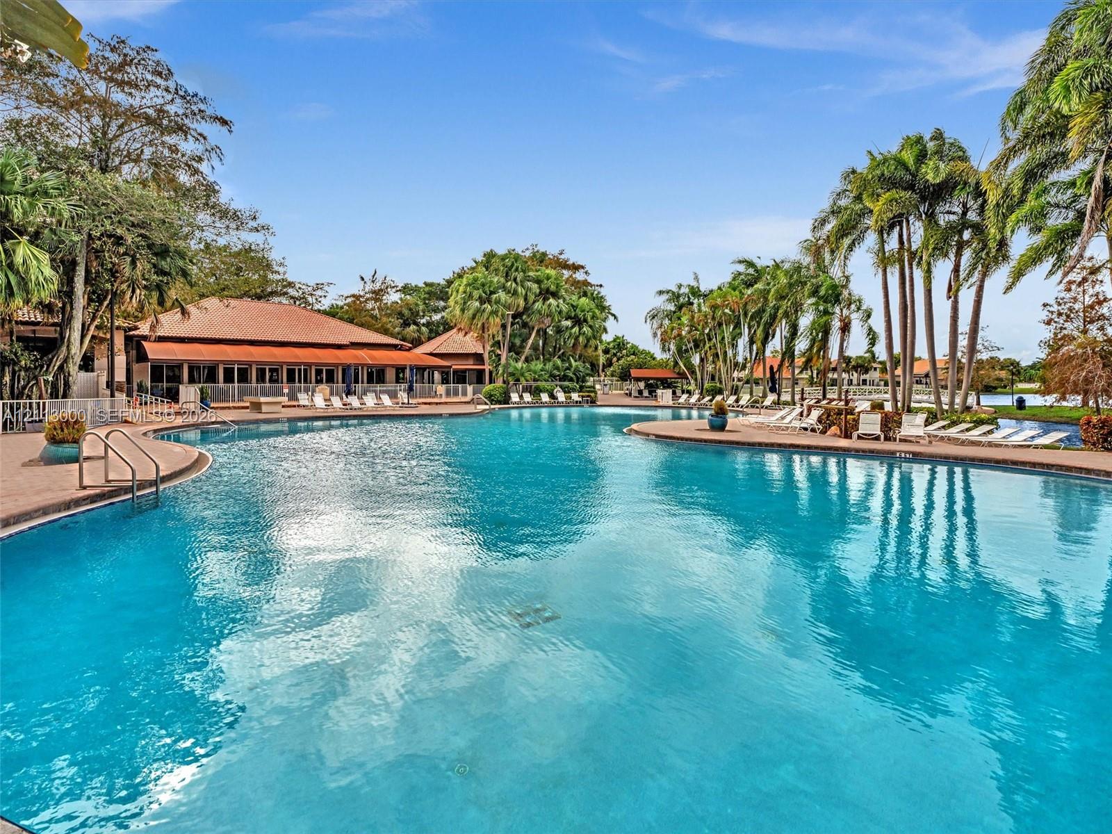 Large free-form swimming pool featuring a tile border, metal handrails, a paved deck, and mature palm trees