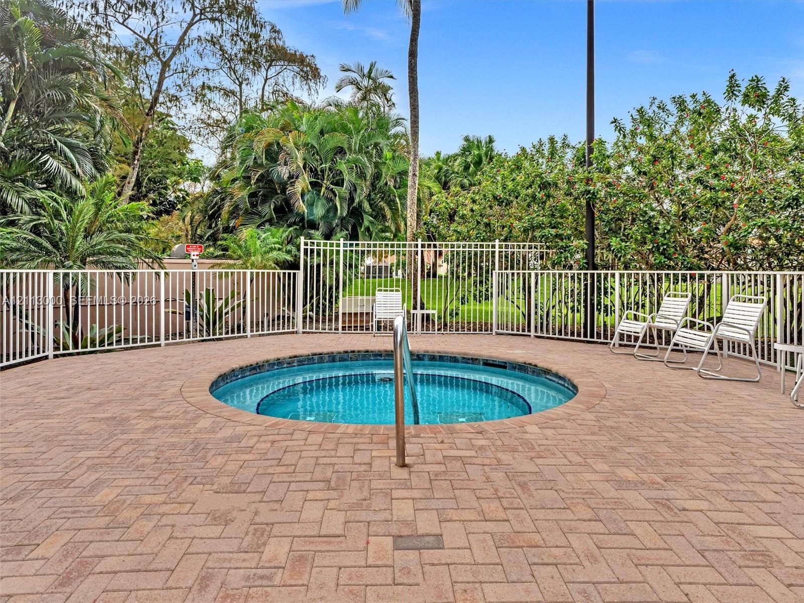 In-ground circular spa featuring a tile finish, metal handrail, brick paver decking in a herringbone pattern, and perimeter metal fencing