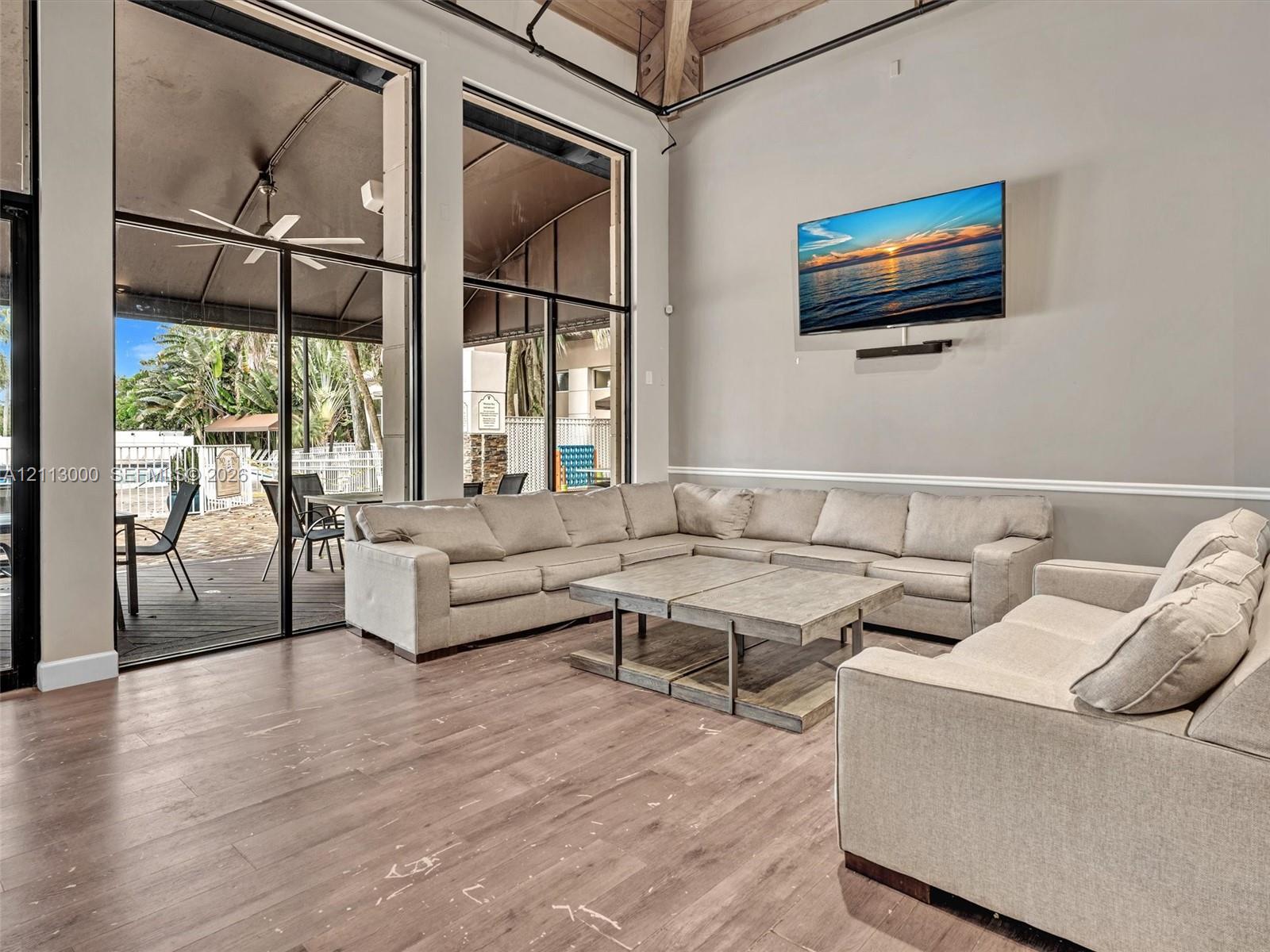 High-ceilinged common area featuring wood-finish flooring, exposed structural beams, floor-to-ceiling windows, and wall-mounted chair rail molding