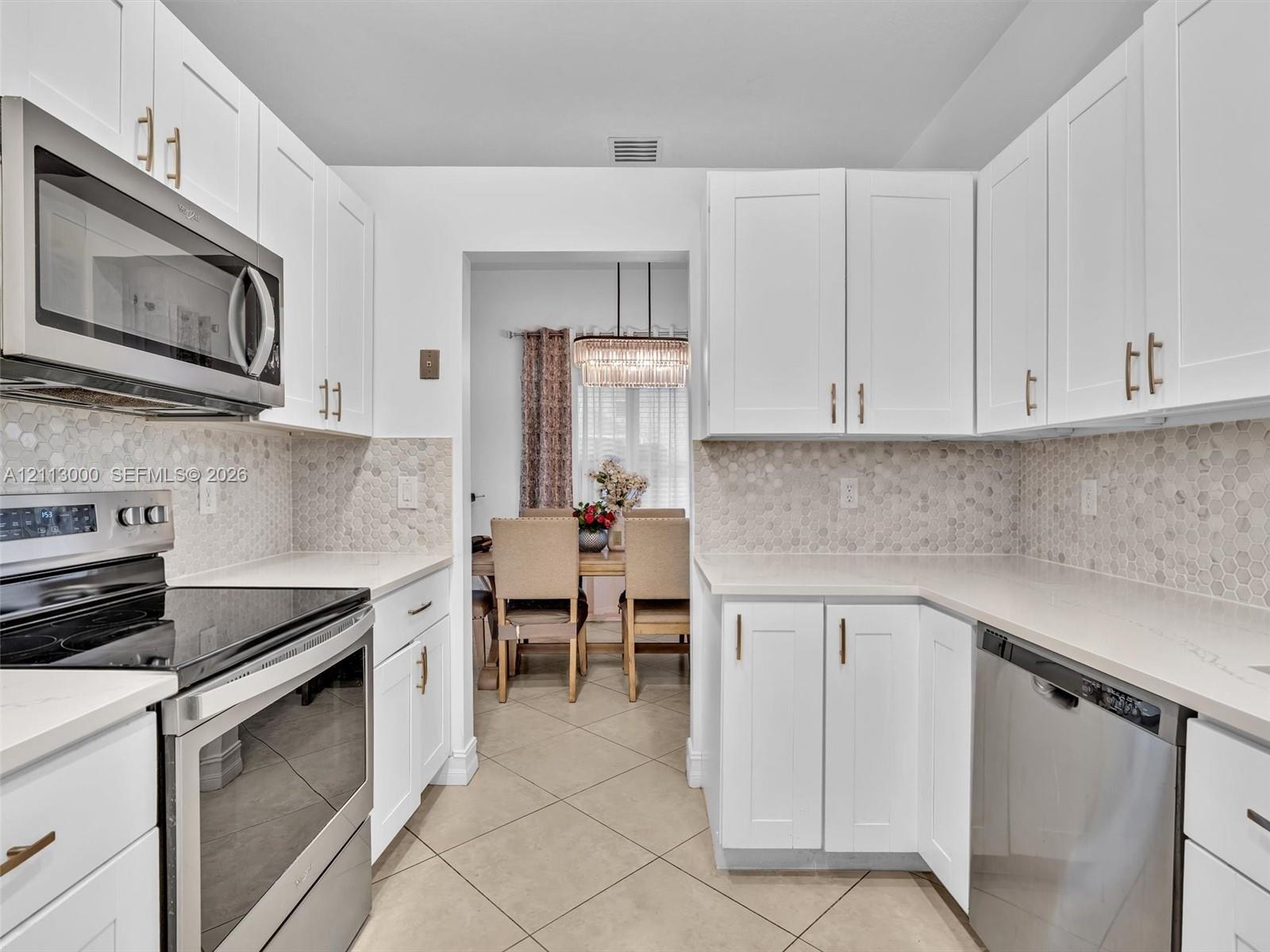 Kitchen featuring white shaker-style cabinetry, stainless steel appliances, neutral stone-finish countertops, and a hexagonal tile backsplash