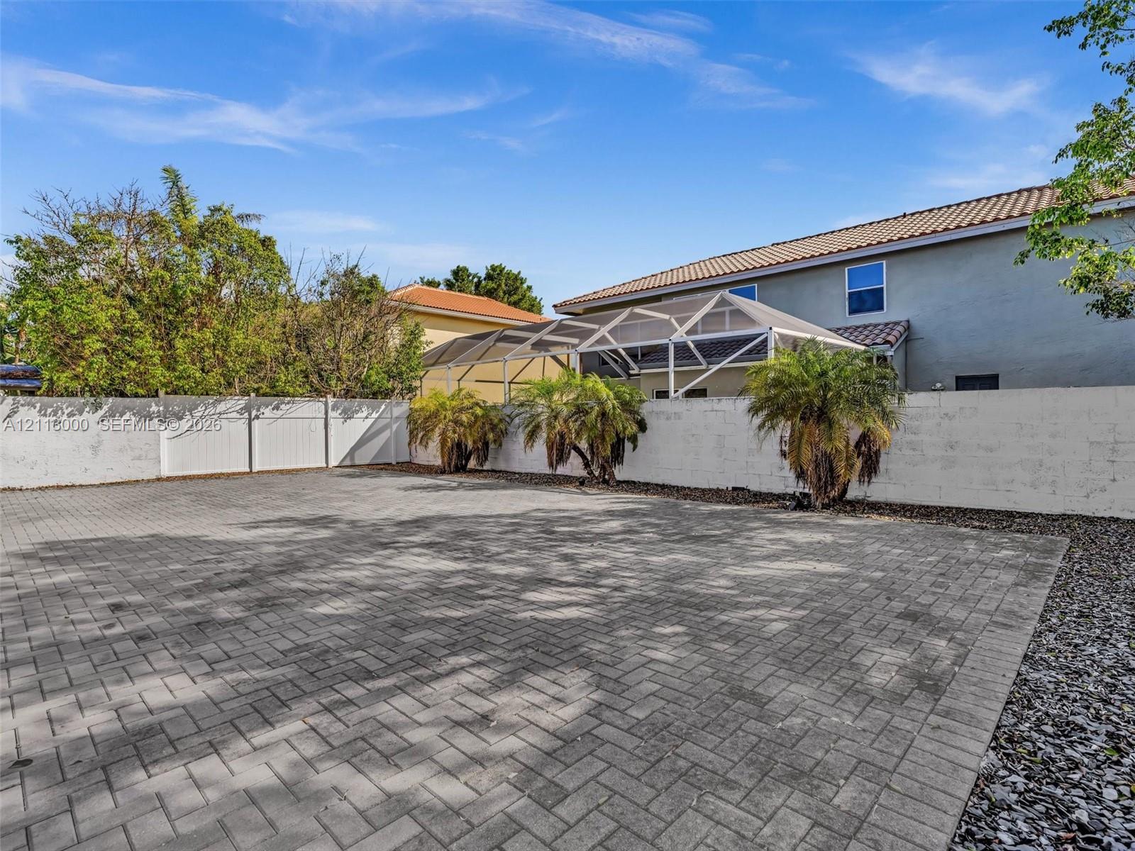 Extensive paver patio featuring a white privacy fence, screen-enclosed patio structure, and mature palm trees