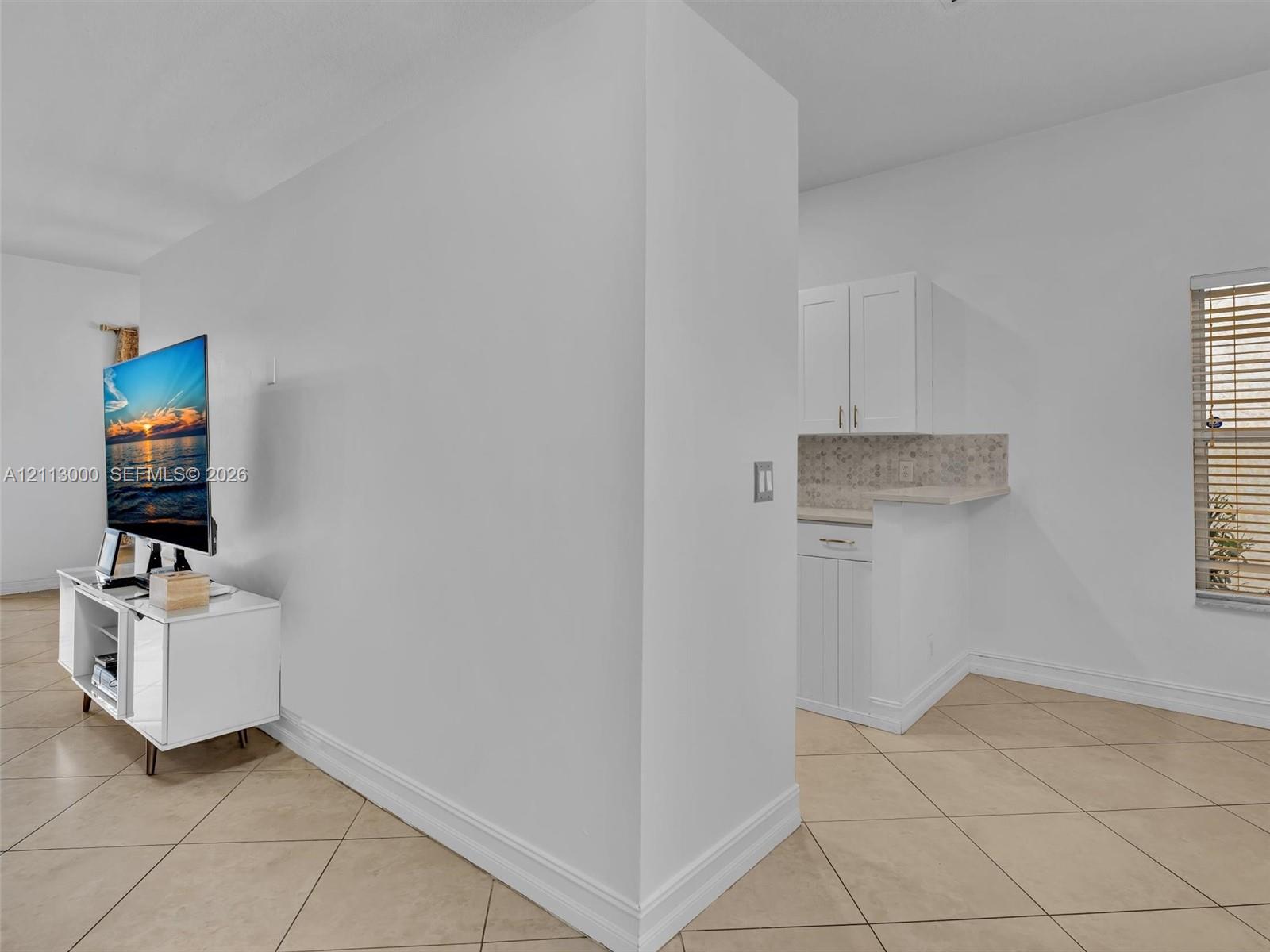 Tile flooring, white Shaker-style cabinetry, neutral stone-finish countertops, and a decorative tile backsplash