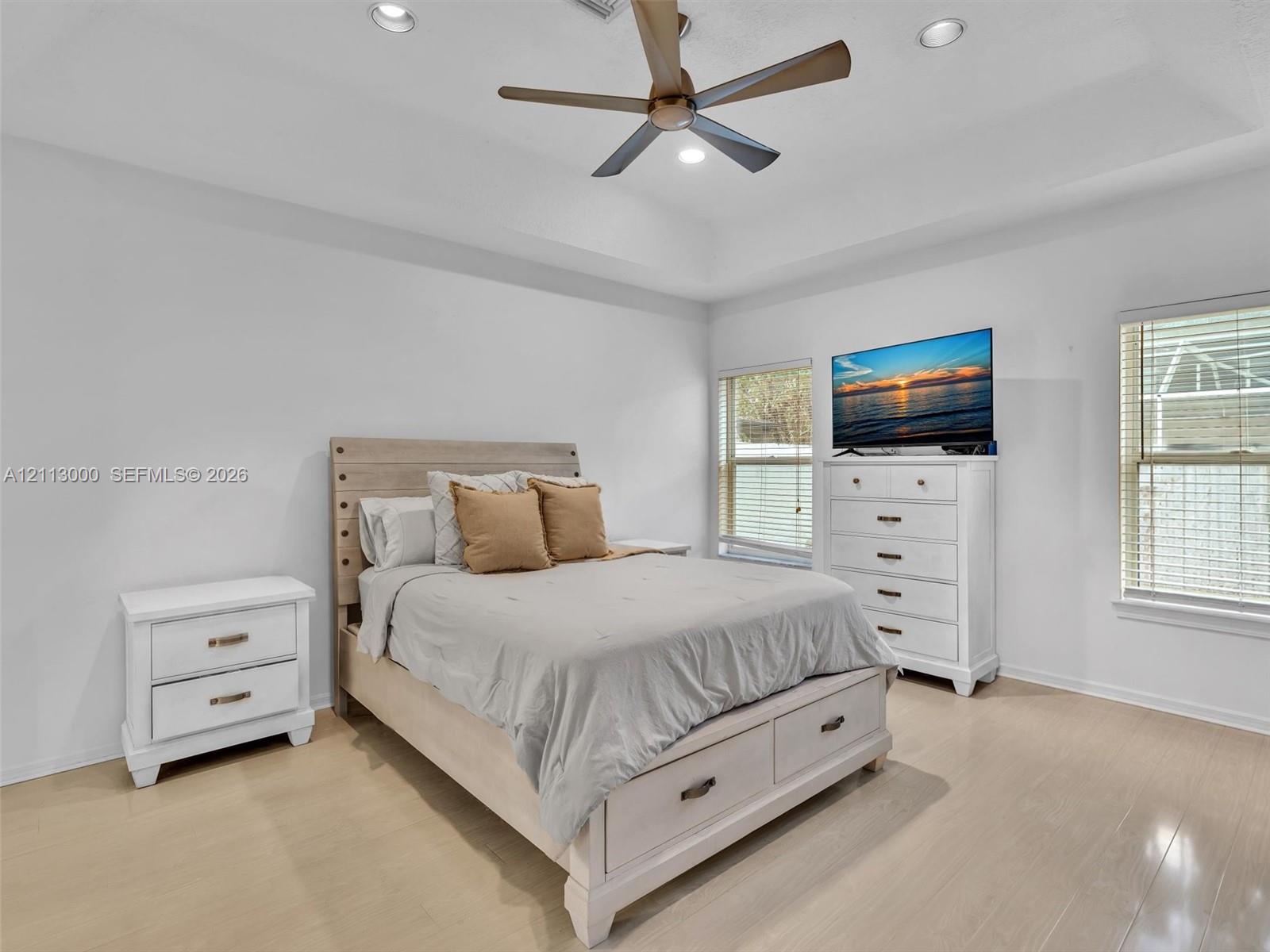Tray ceiling with recessed lighting, multi-blade ceiling fan, and light-toned wood-finish flooring