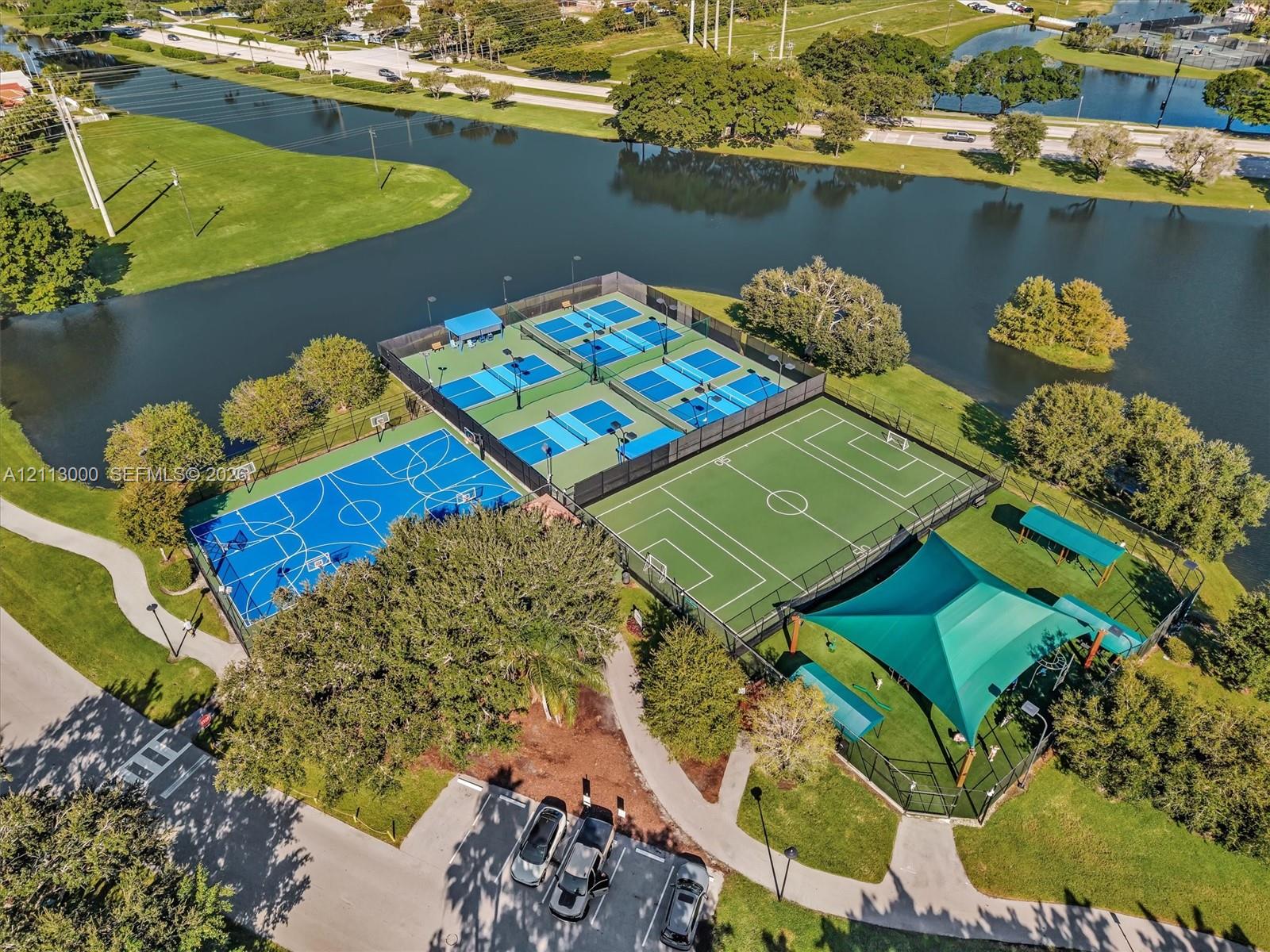 Recreational complex featuring four fenced tennis courts, a basketball court, a multi-use turf field, and a shaded pavilion