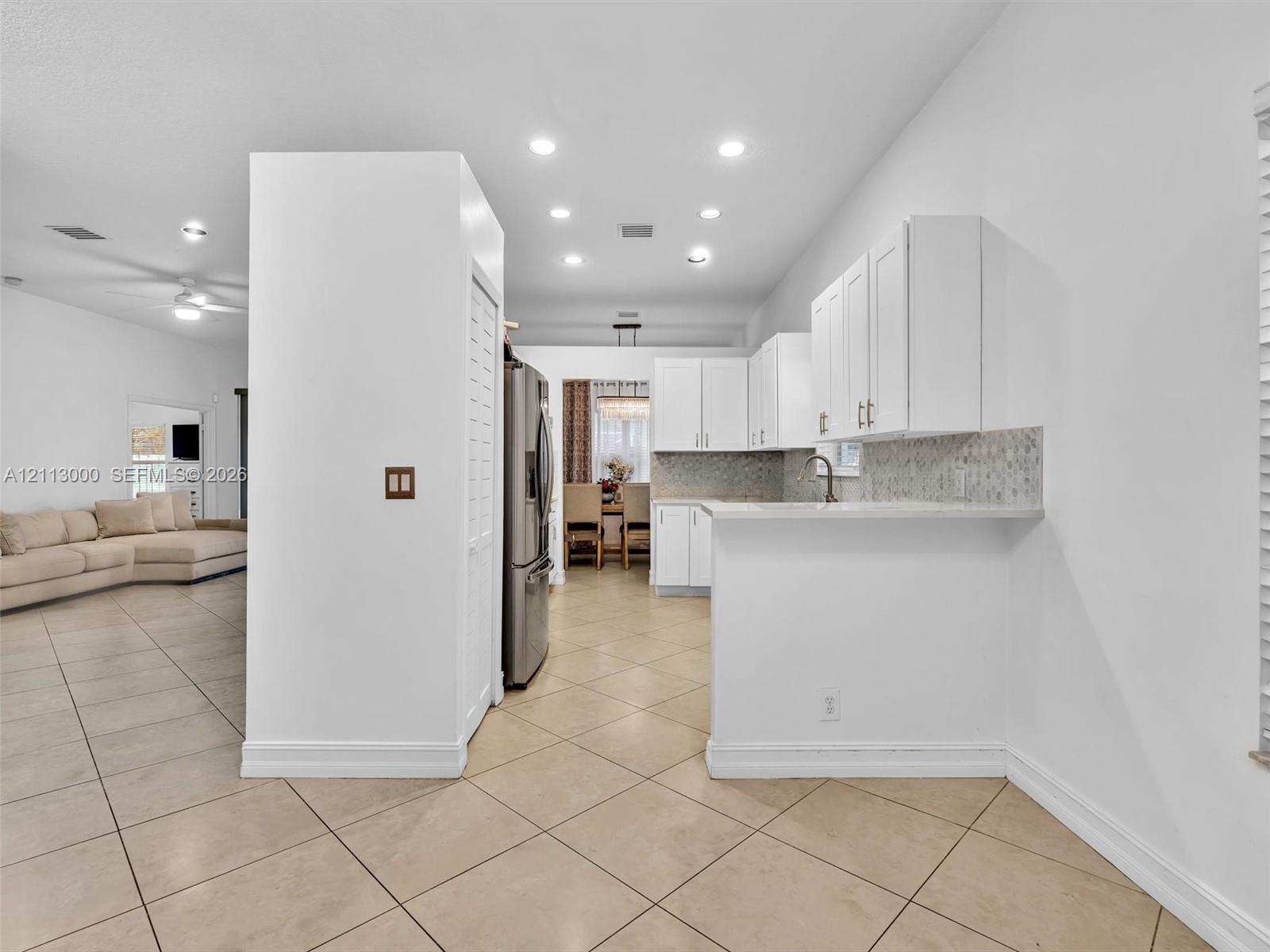 Kitchen featuring white cabinetry, solid-surface countertops, tile backsplash, stainless steel refrigerator, and recessed lighting