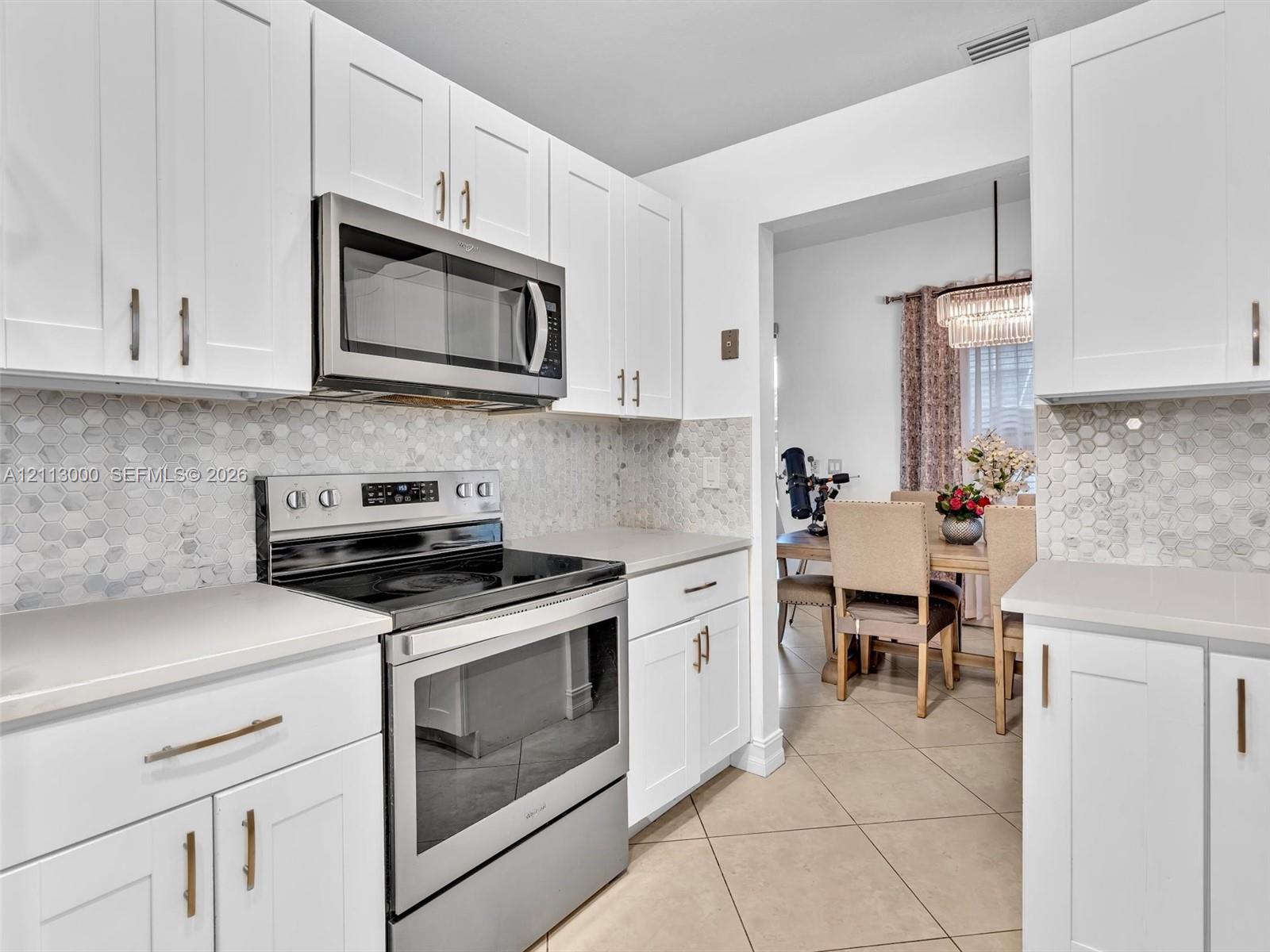 Kitchen featuring white Shaker-style cabinetry, stainless steel appliances, hexagonal tile backsplash, solid-surface countertops, and tile flooring