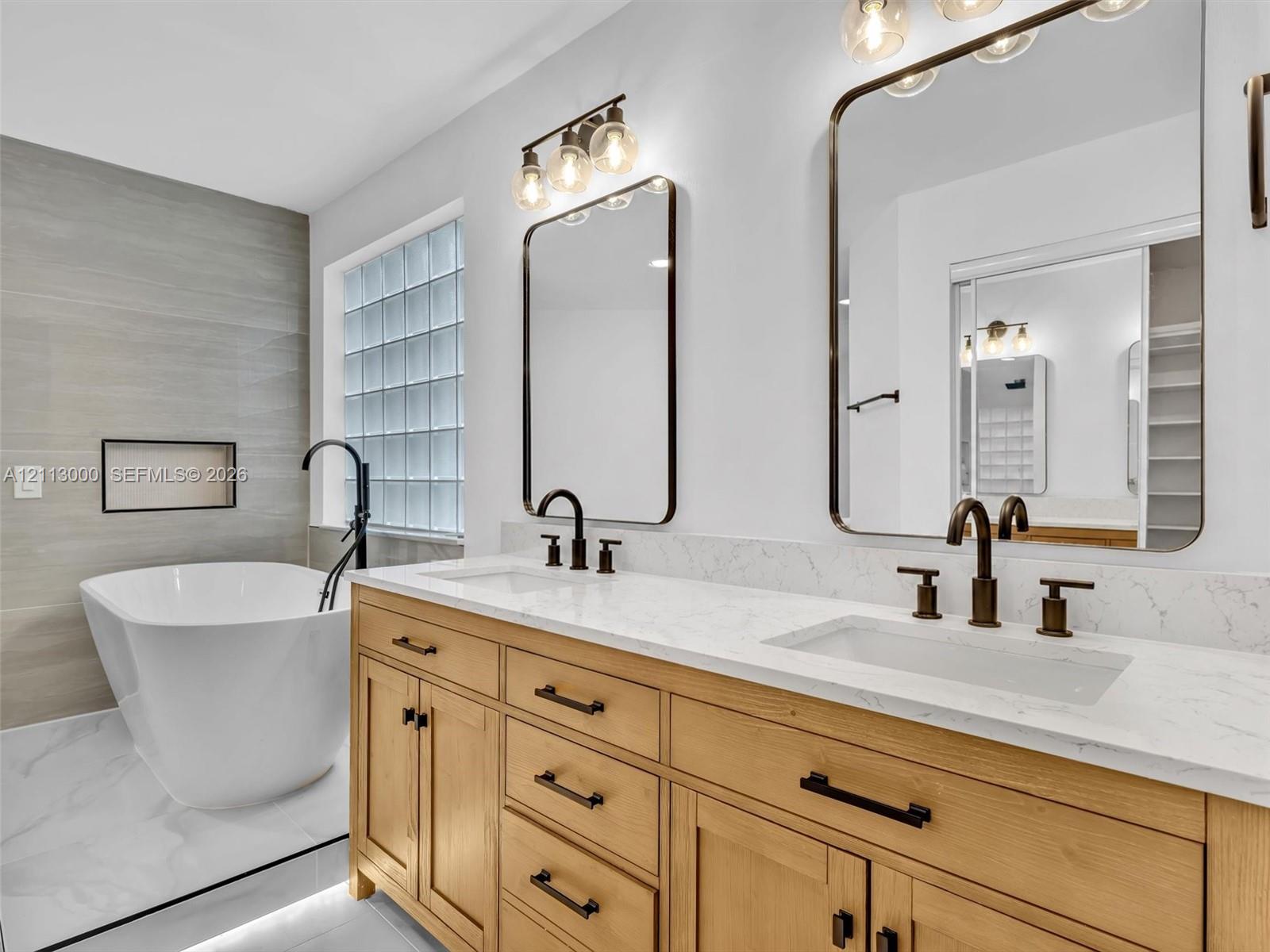 Double vanity featuring natural wood cabinetry, white stone-composite countertops, rectangular undermount sinks, and matte black fixtures