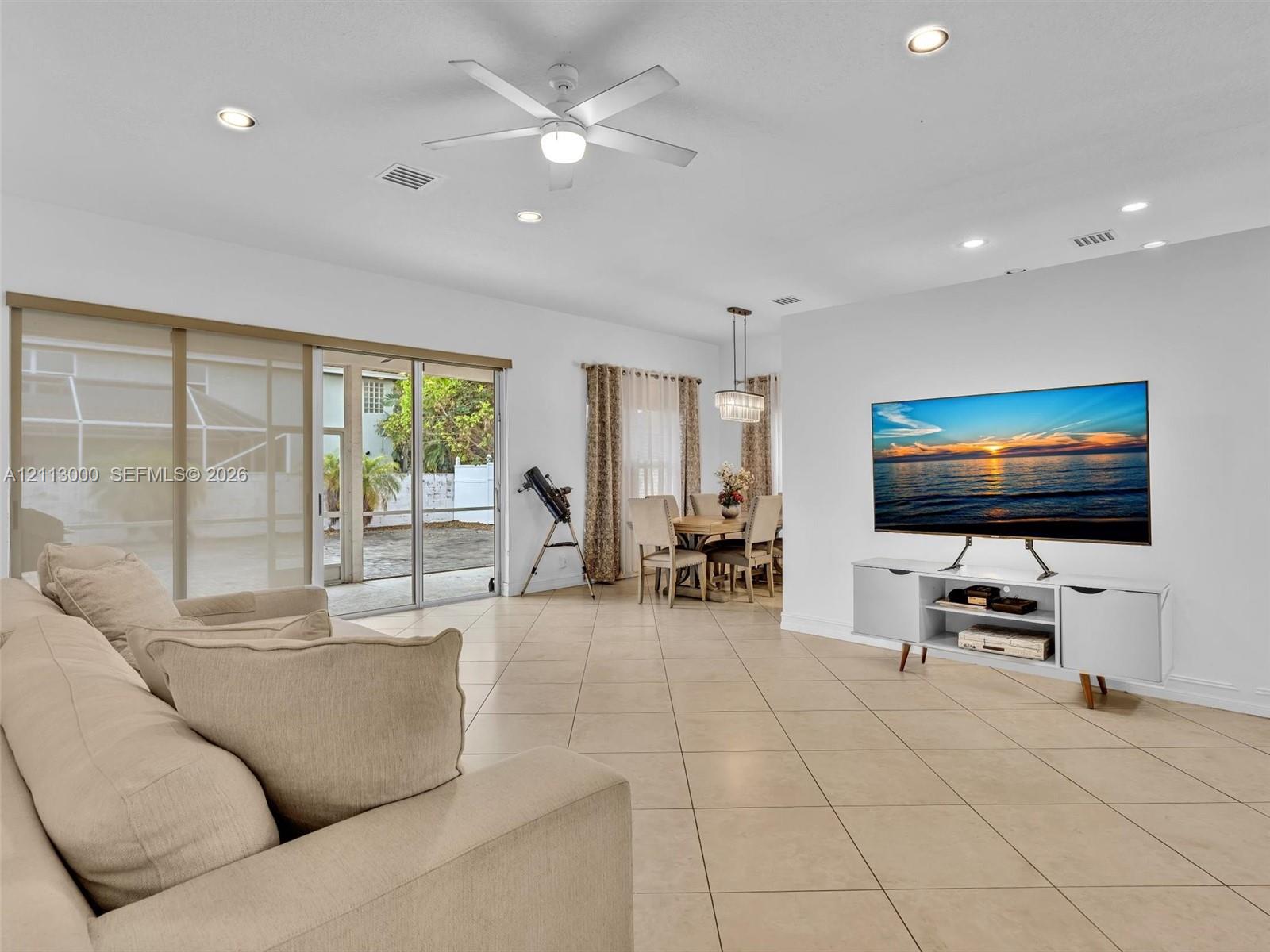 Large-format neutral tile flooring, recessed ceiling lighting, central ceiling fan, and expansive sliding glass doors