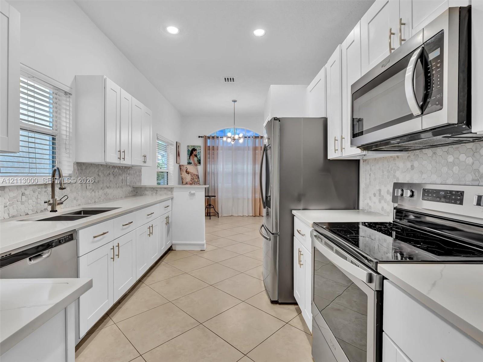Kitchen featuring white shaker-style cabinetry, stainless steel appliances, quartz countertops, hexagonal mosaic tile backsplash, and tile flooring